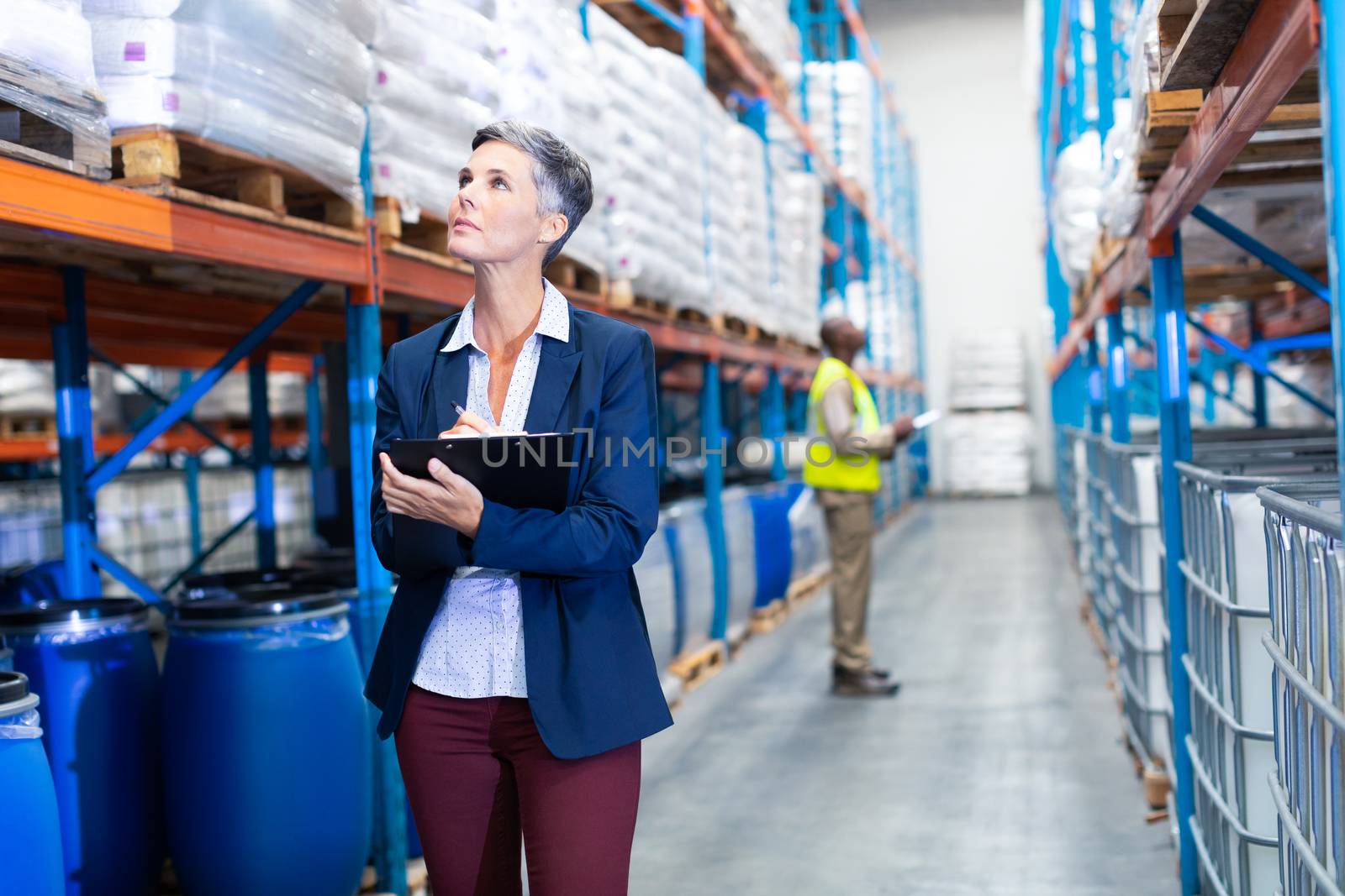 Front view of beautiful mature Caucasian female manager checking stocks on clipboard in warehouse. This is a freight transportation and distribution warehouse. Industrial and industrial workers concept