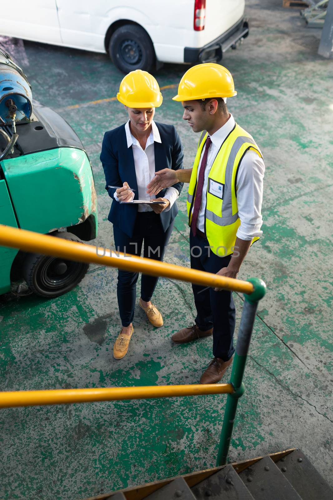 High angle view of Caucasian female manager and Caucasian male supervisor discussing over clipboard in warehouse. This is a freight transportation and distribution warehouse. Industrial and industrial workers concept