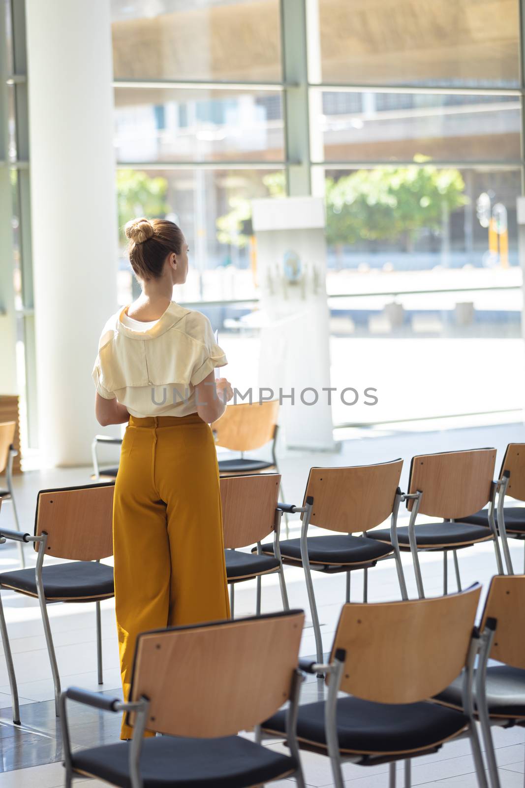 Rear view of young Caucasian female executive looking away while standing in empty conference room