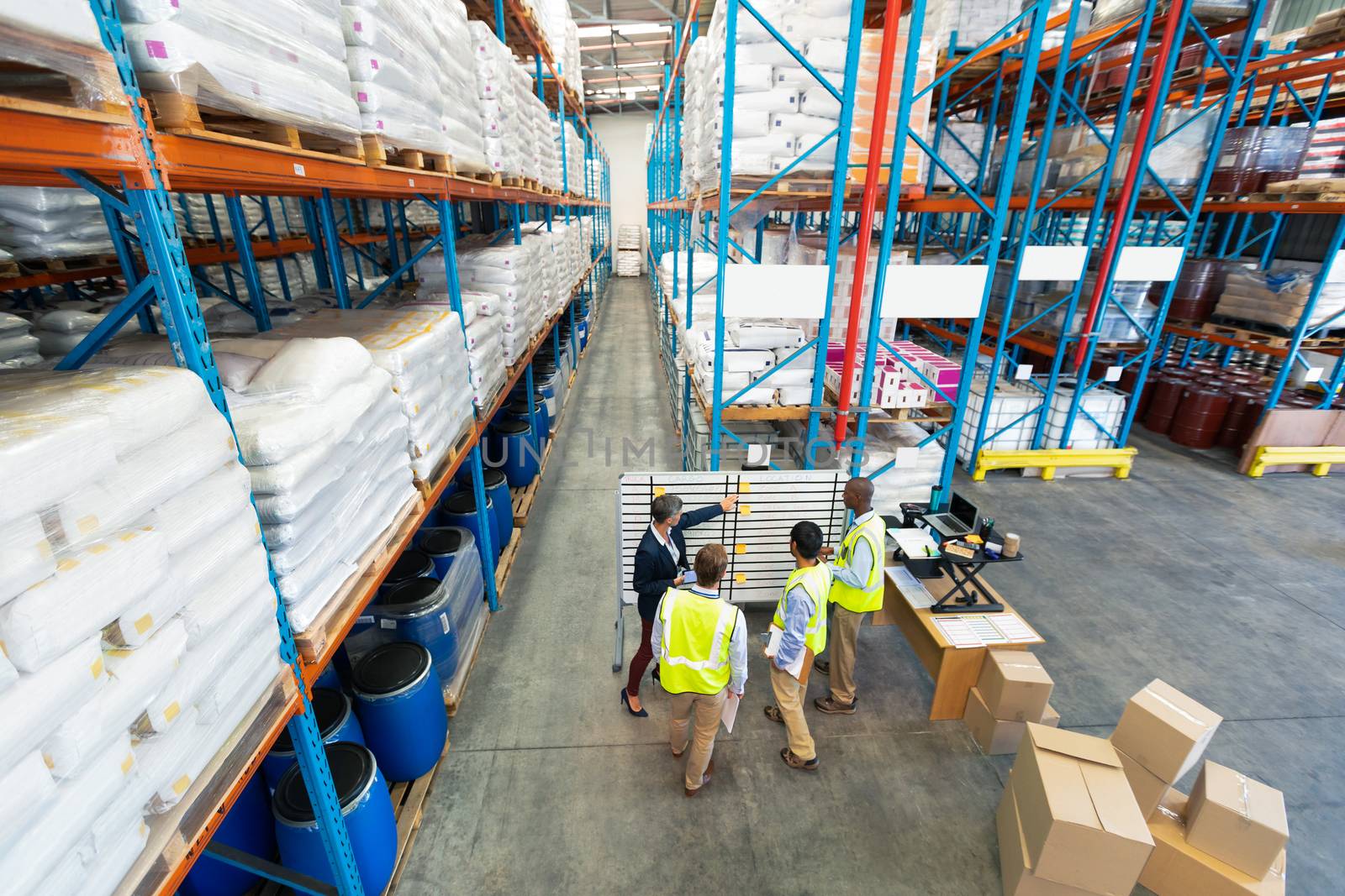 High angle view of mature diverse warehouse staff discussing over whiteboard in warehouse. This is a freight transportation and distribution warehouse. Industrial and industrial workers concept