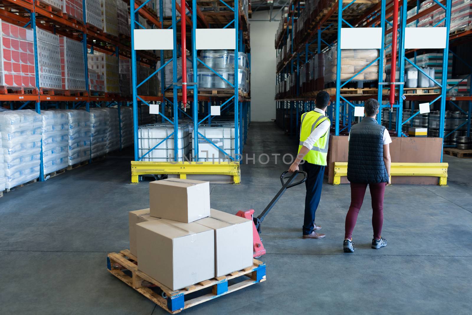 Rear view of Caucasian Male staff with his coworker using pallet jack in warehouse. This is a freight transportation and distribution warehouse. Industrial and industrial workers concept
