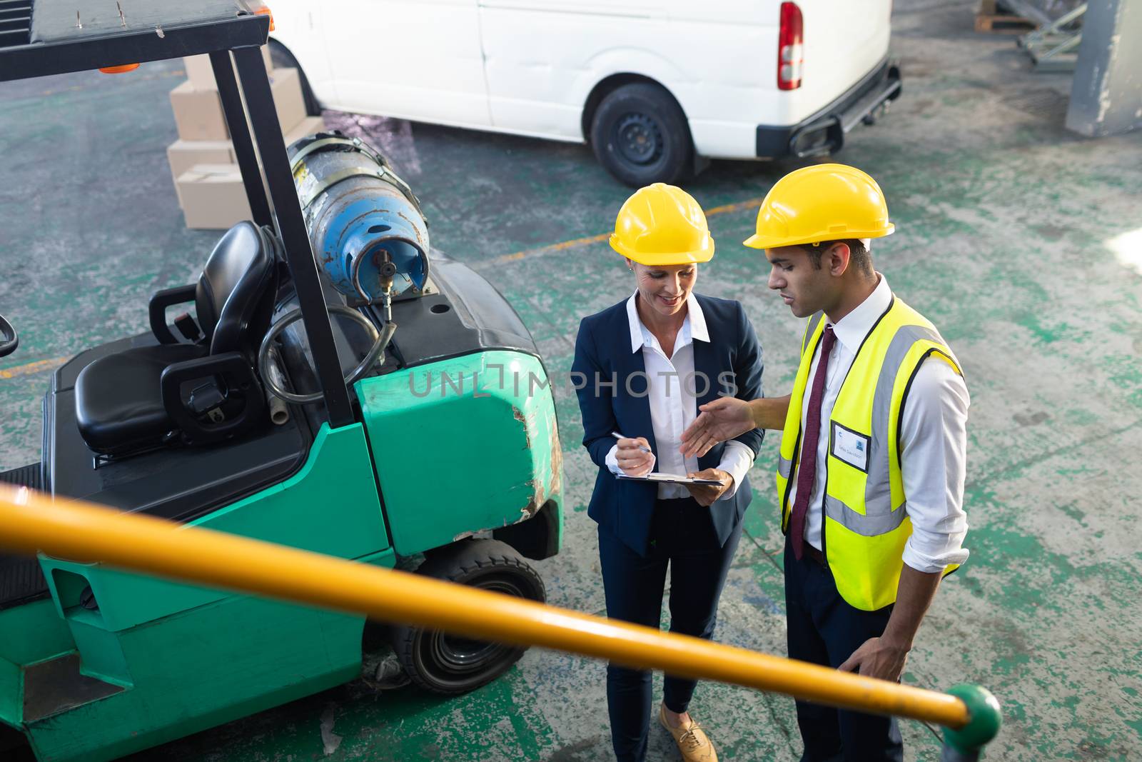 High angle view of Caucasian female manager and Caucasian male supervisor discussing over clipboard in warehouse. This is a freight transportation and distribution warehouse. Industrial and industrial workers concept