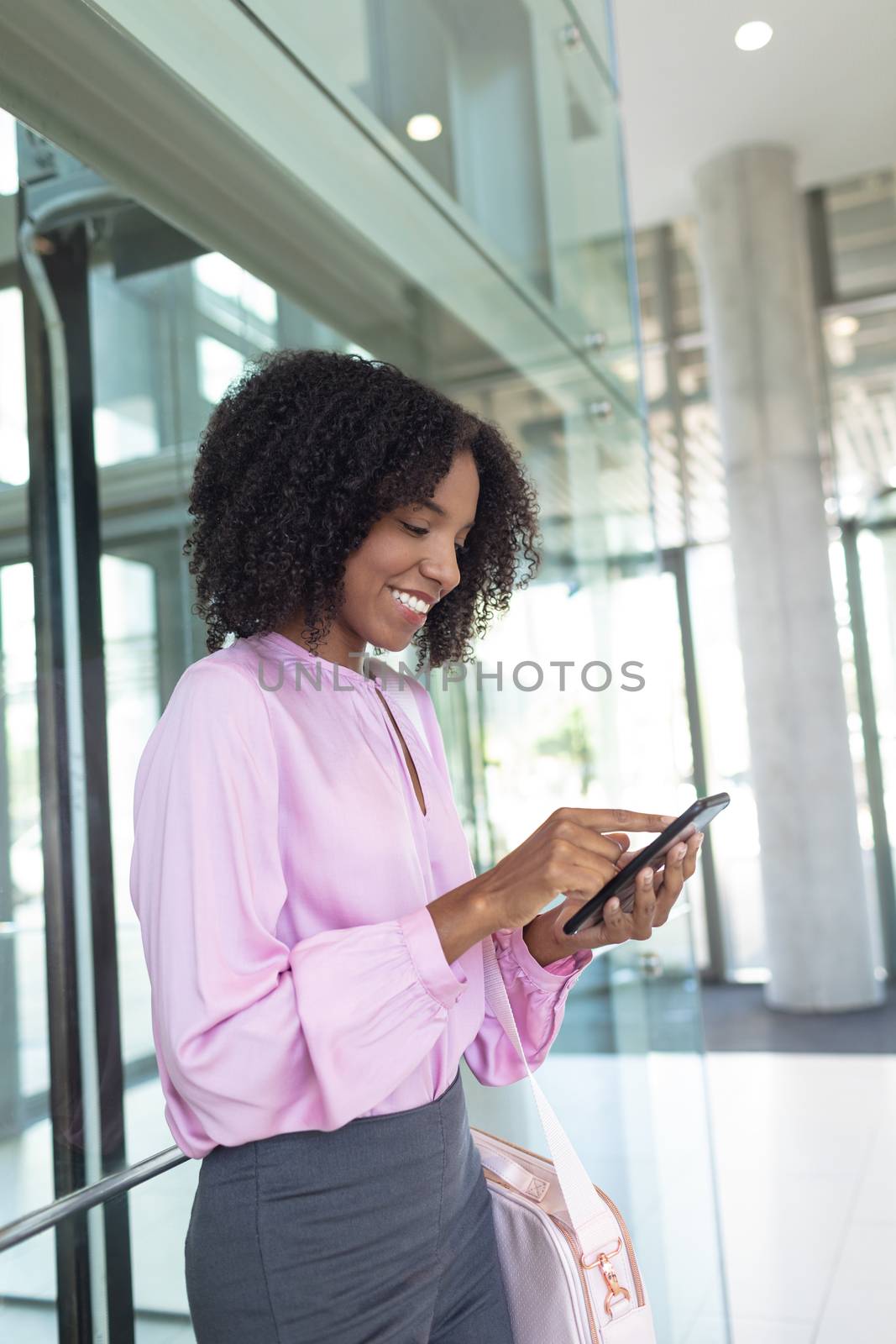 Side view of African american female executive looking at mobile phone while waiting the lift in modern office