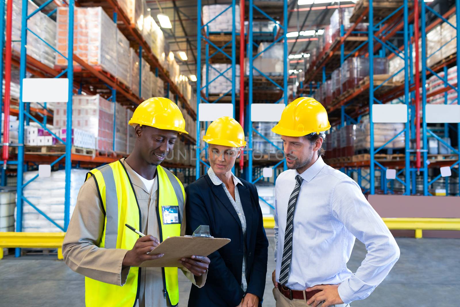 Front view of diverse mature staffs working together on clipboard in warehouse. This is a freight transportation and distribution warehouse. Industrial and industrial workers concept