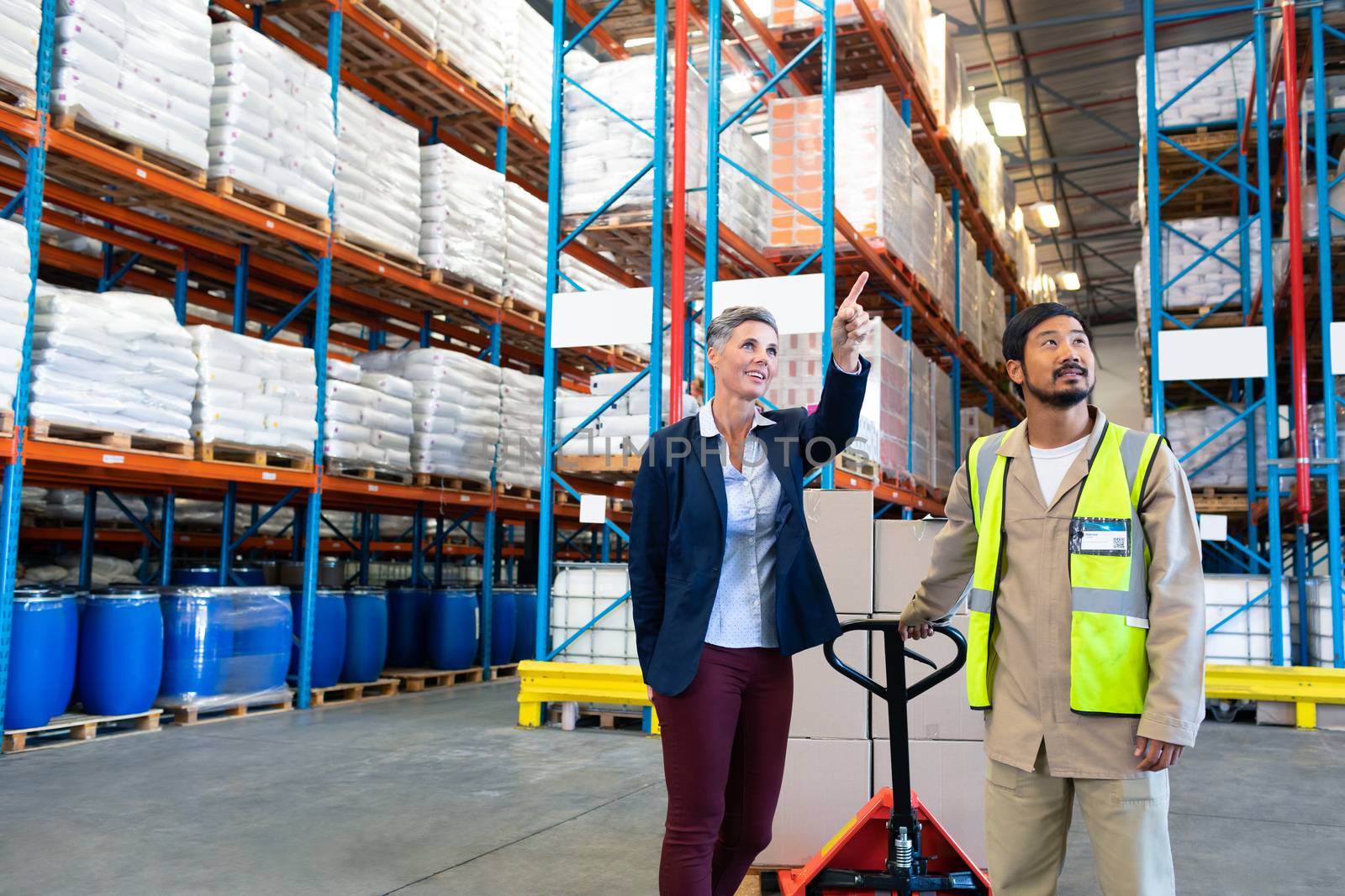 Female manager standing with worker and pointing at distance in warehouse by Wavebreakmedia