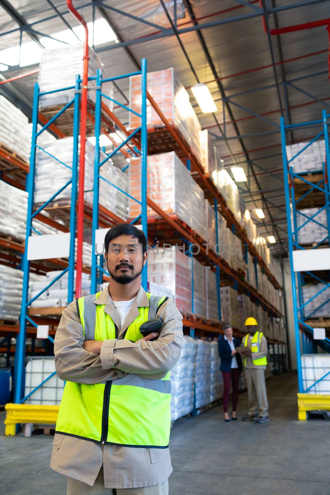 Front view of confident handsome Asian male worker standing with arms crossed and looking at camera in warehouse. This is a freight transportation and distribution warehouse. Industrial and industrial workers concept