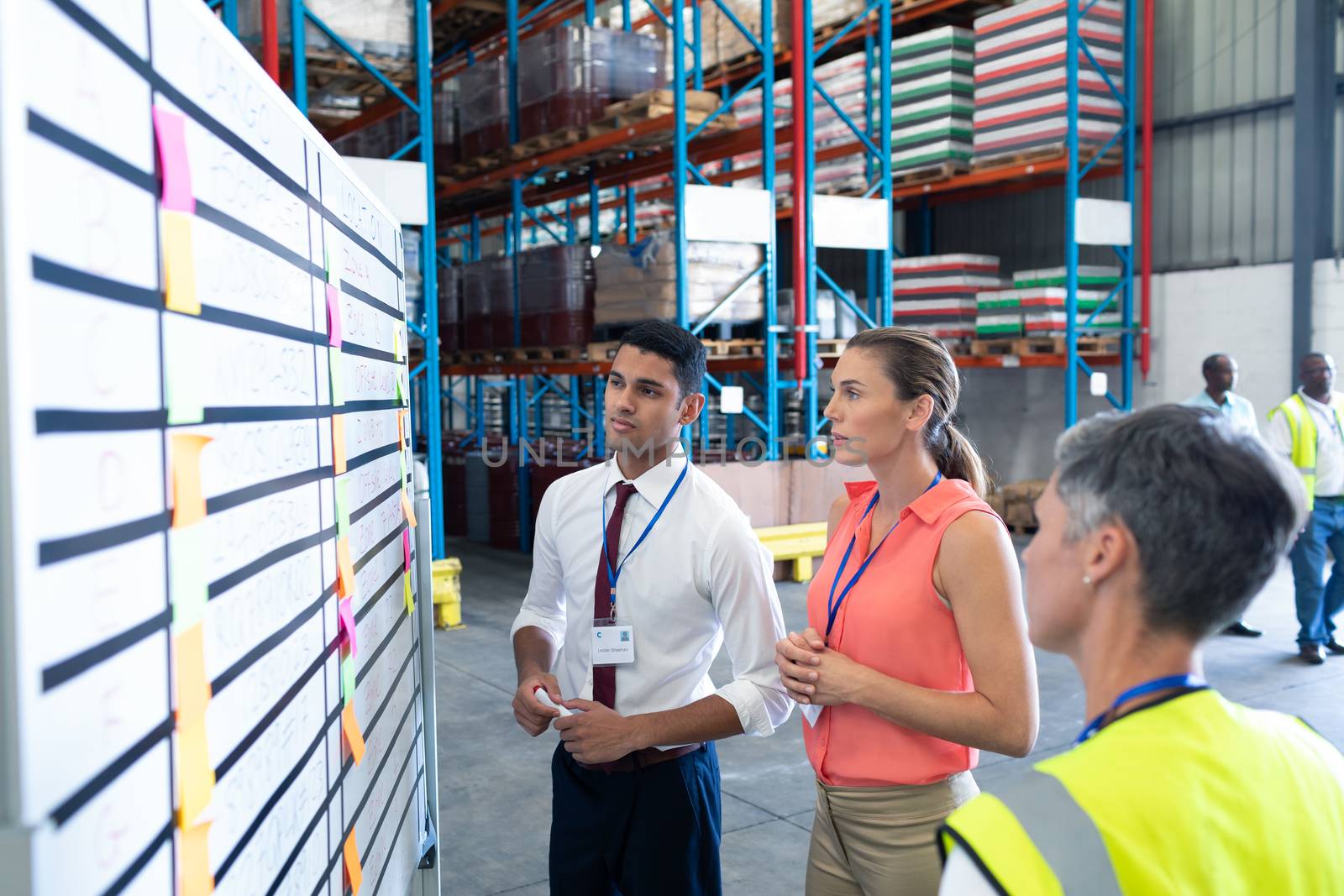 Front view of diverse warehouse staffs looking at whiteboard in warehouse. This is a freight transportation and distribution warehouse. Industrial and industrial workers concept