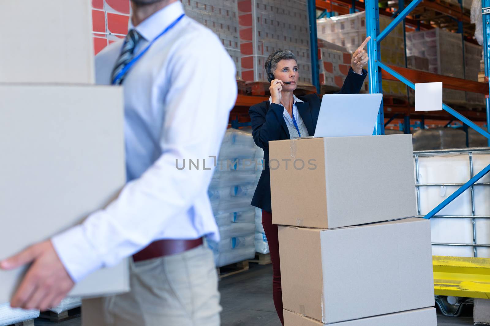 Female manager with laptop talking on headset in warehouse by Wavebreakmedia
