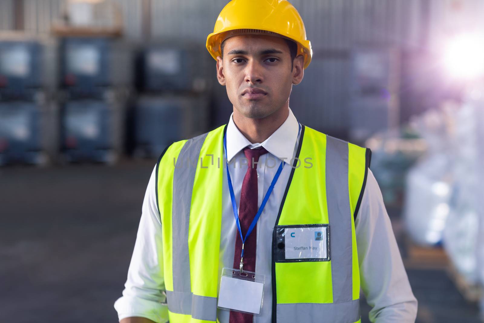 Male staff in hardhat and reflective jacket standing in warehouse by Wavebreakmedia