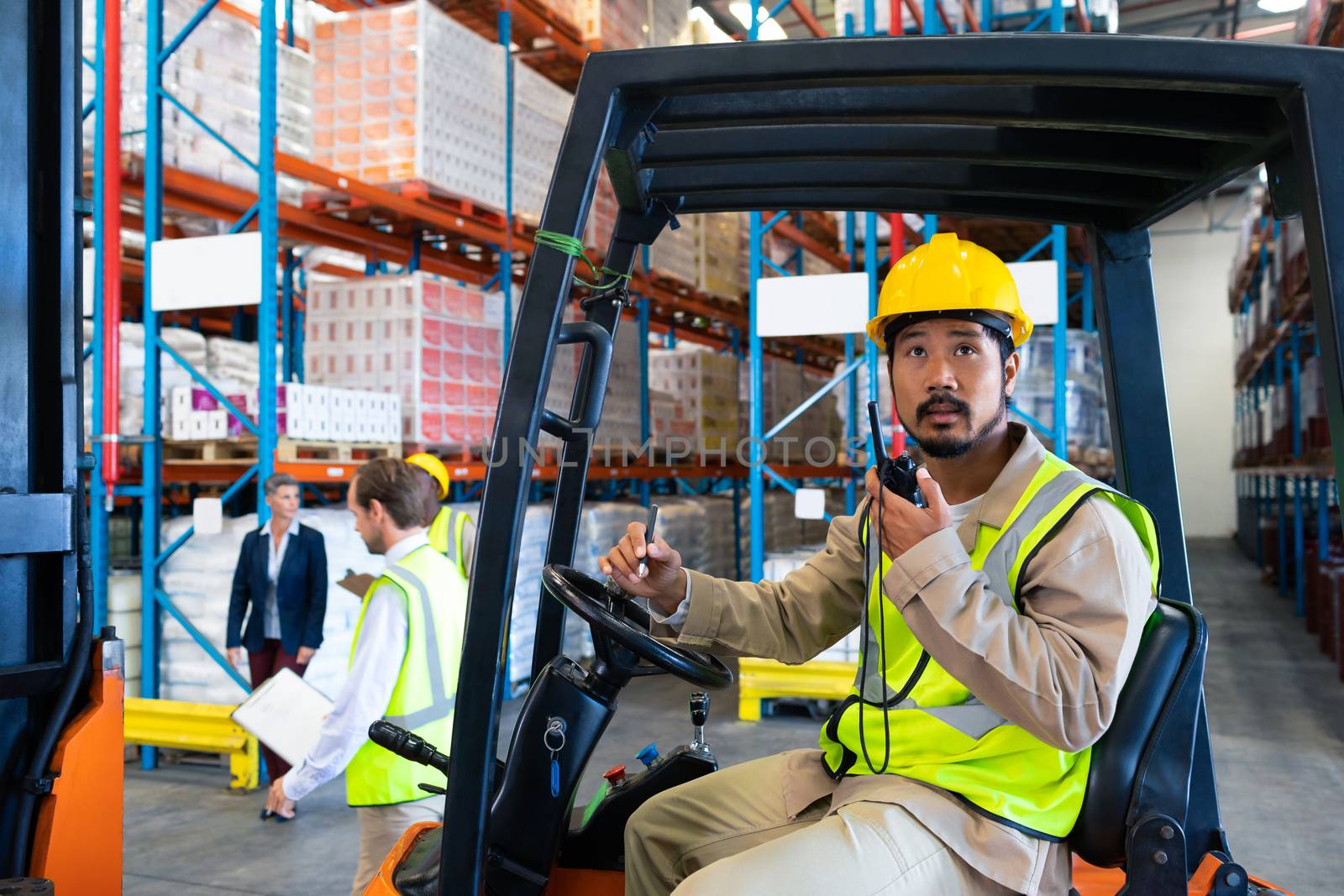 Male worker talking on walkie-talkie while driving forklift in warehouse by Wavebreakmedia