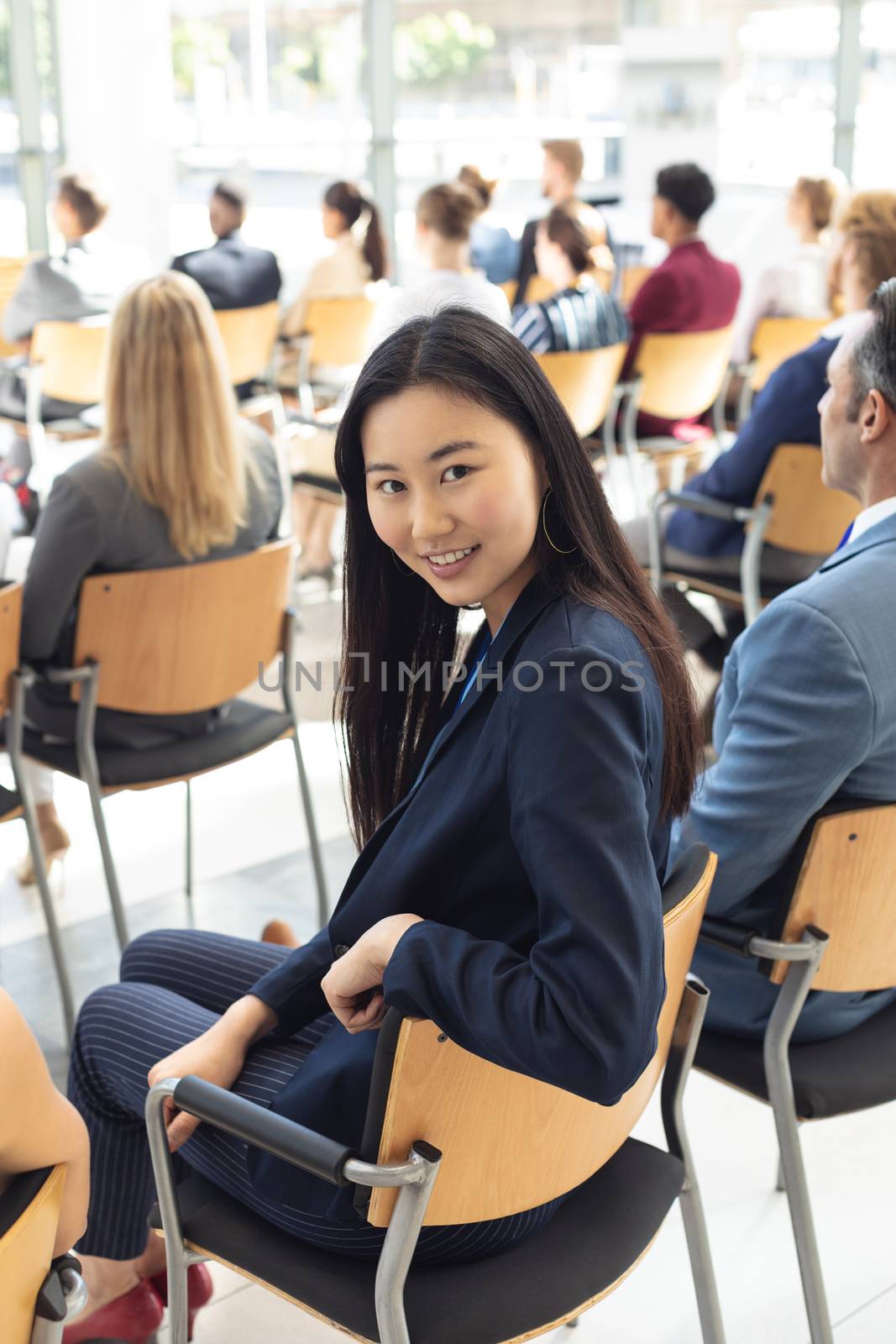 Side view of young Asian businesswoman sat in conference room, smiling to camera
