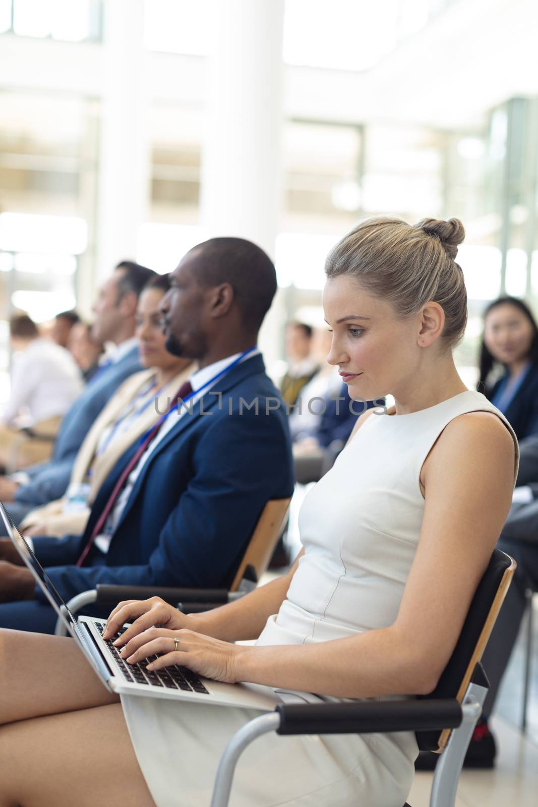 Side view of young Caucasian female executive using laptop in conference room. Executives in the background. 