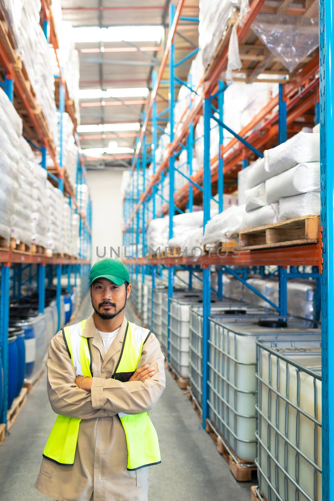 Front view of confident mature Asian male worker standing with arms crossed and looking at camera in warehouse. This is a freight transportation and distribution warehouse. Industrial and industrial workers concept