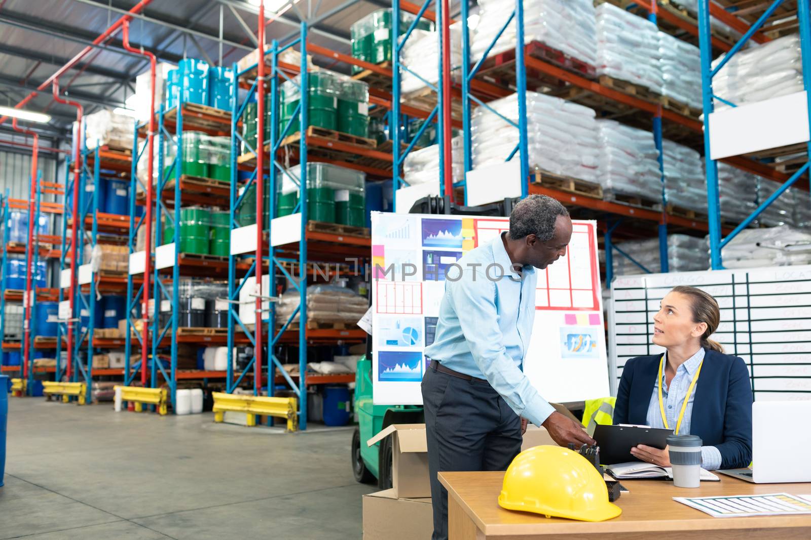 Front view of mature diverse male and female staffs discussing over clipboard at desk in warehouse. This is a freight transportation and distribution warehouse. Industrial and industrial workers concept