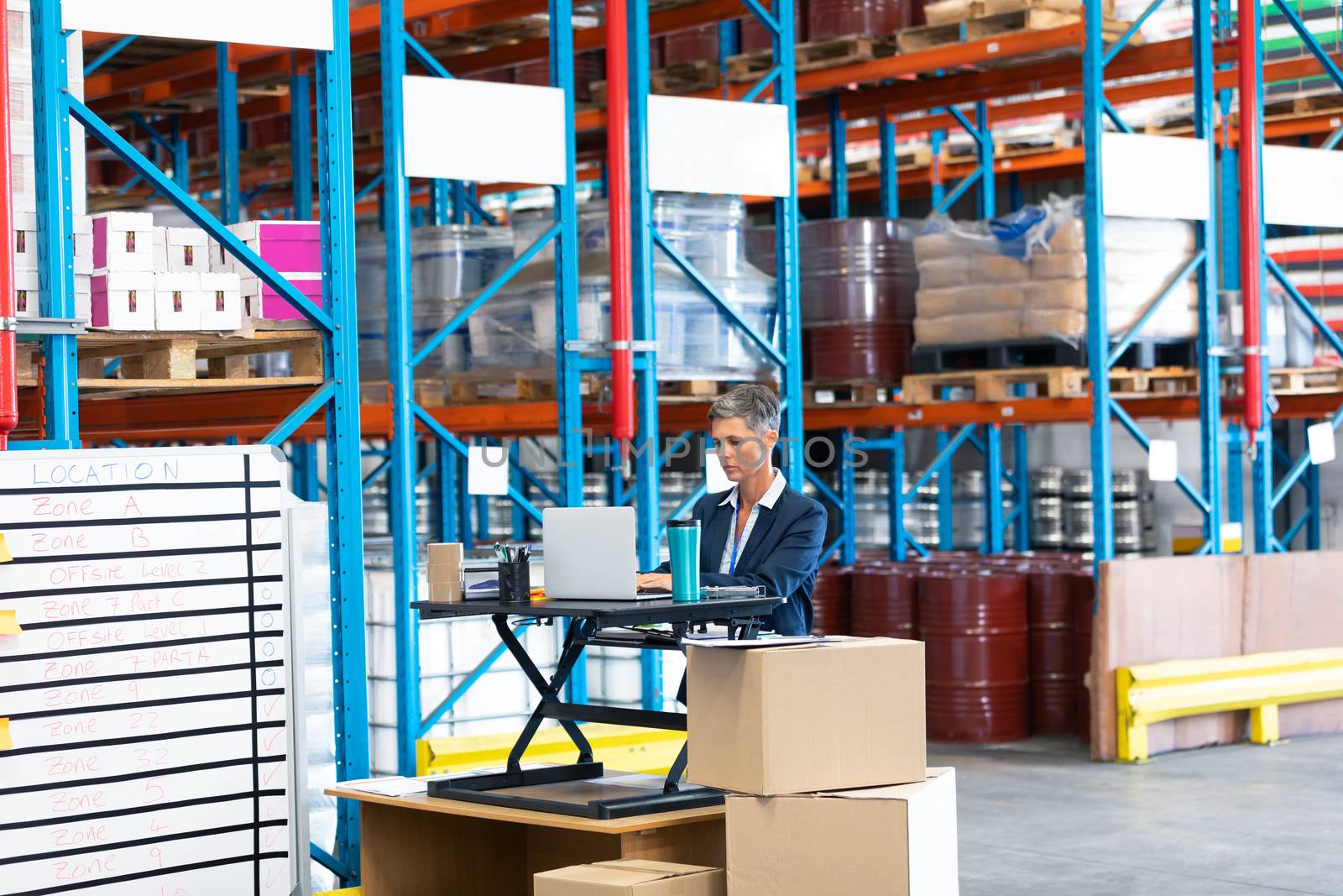 Front view of beautiful mature Caucasian female manager working at desk in workhouse. This is a freight transportation and distribution warehouse. Industrial and industrial workers concept