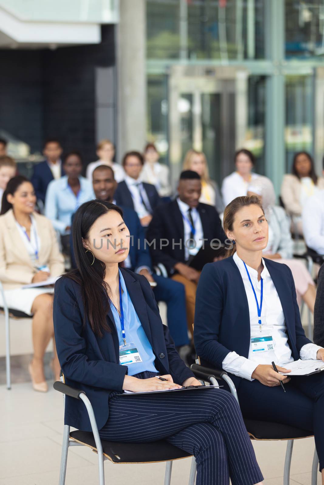 Front view of diverse business people sitting on chairs while listening to speech in conference room
