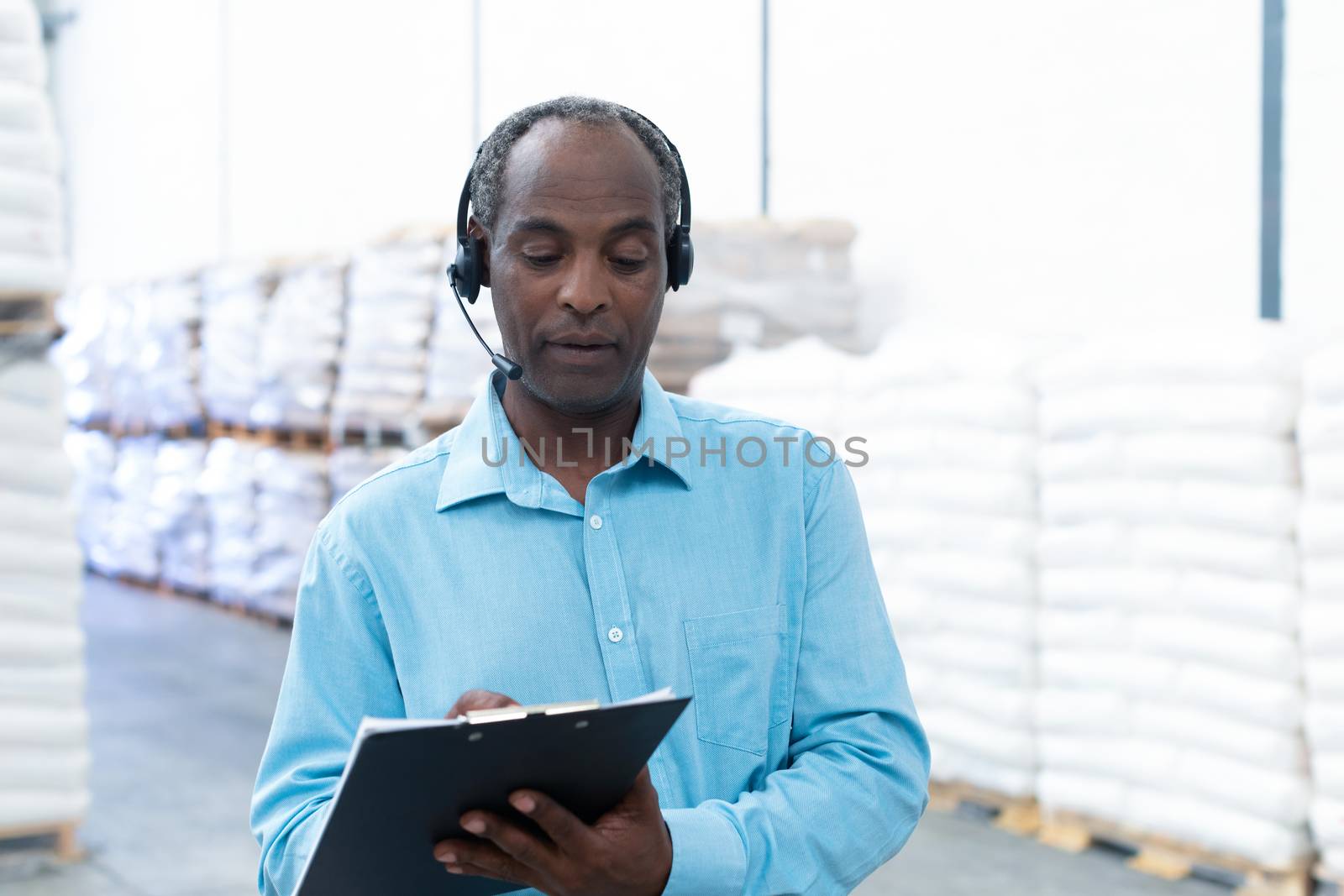 Front view handsome mature African-american male supervisor writing on clipboard in warehouse. This is a freight transportation and distribution warehouse. Industrial and industrial workers concept