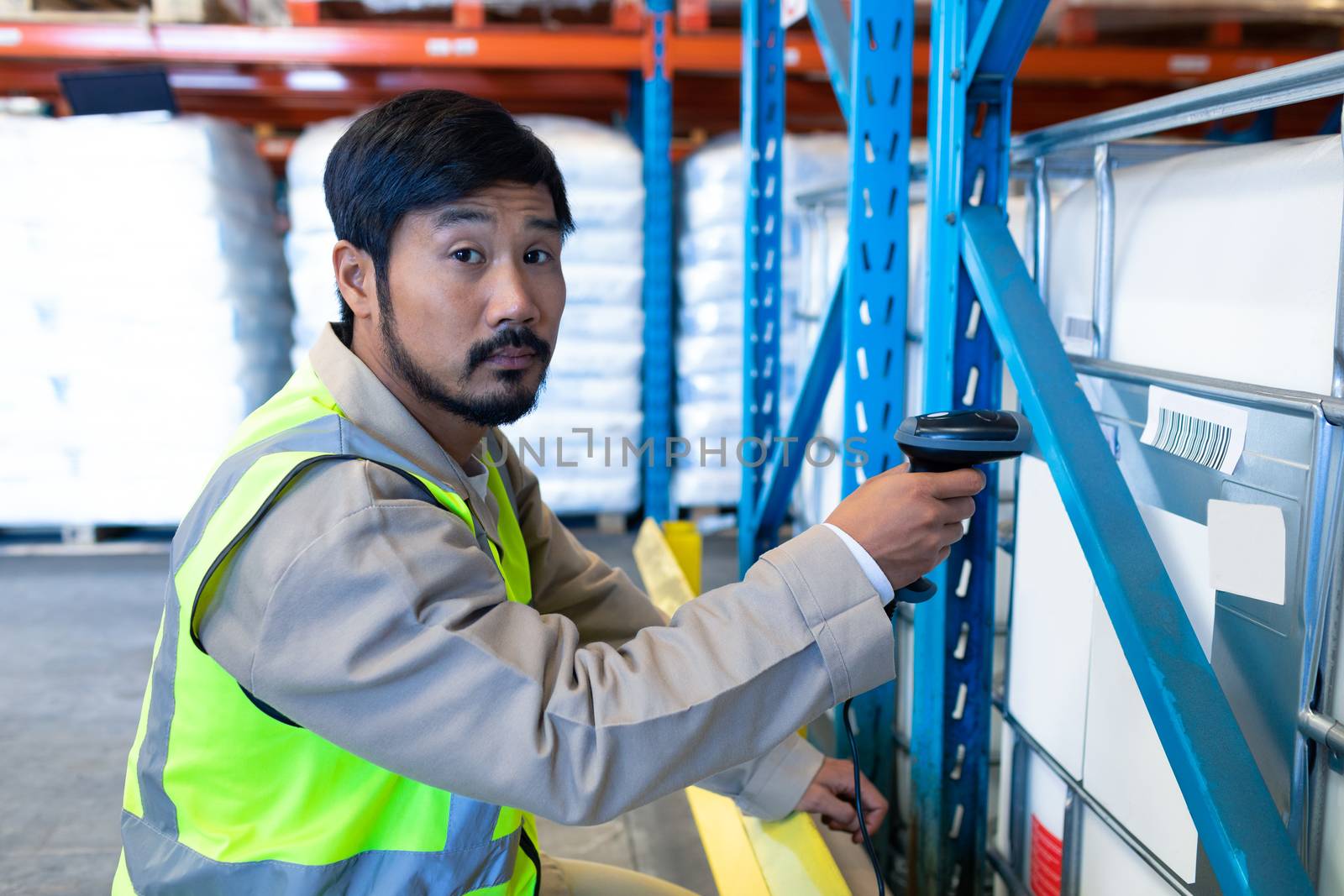 Side view of mature Asian male worker looking at camera while scanning package in modern warehouse. This is a freight transportation and distribution warehouse. Industrial and industrial workers concept
