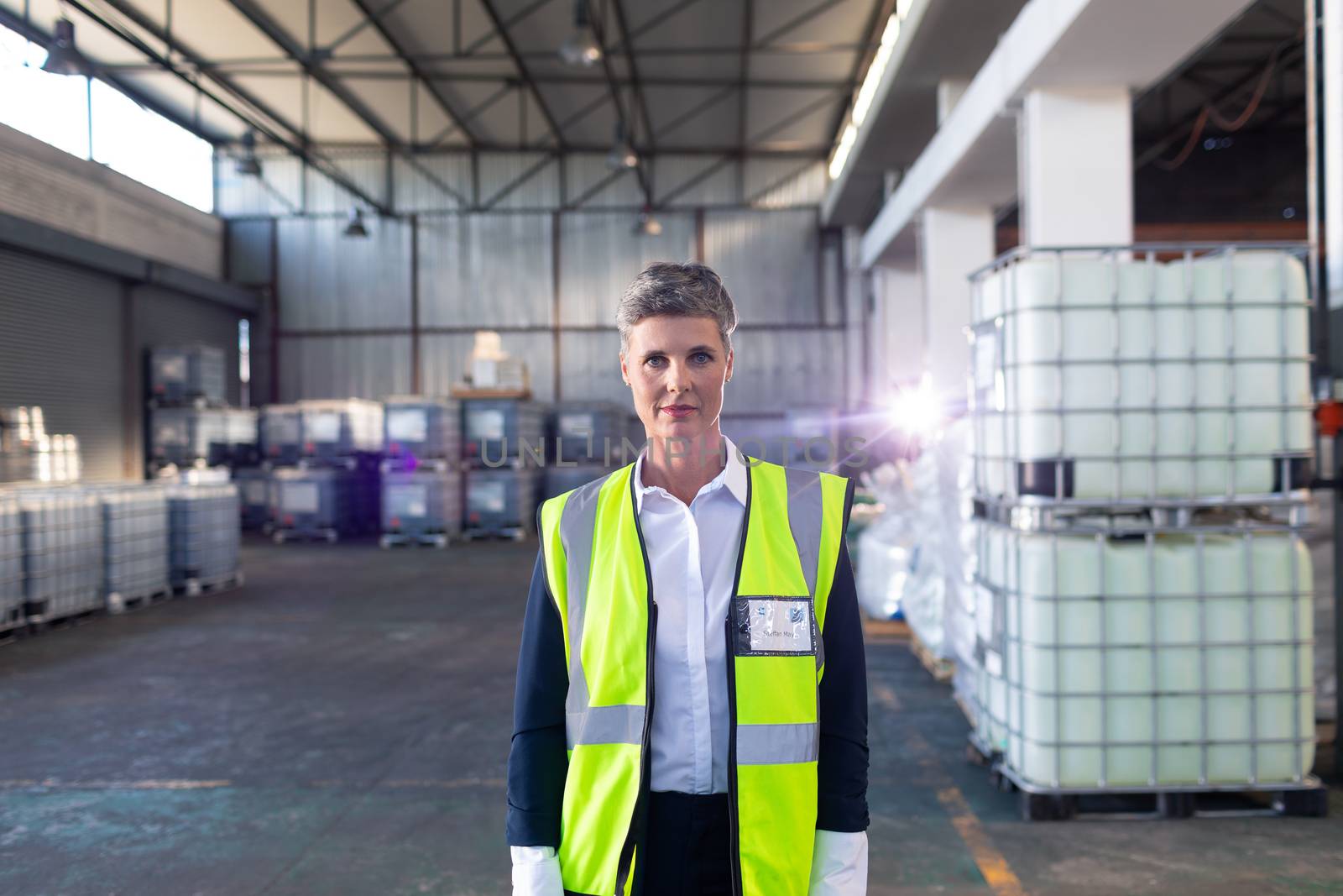 Portrait of Caucasian mature female staff in reflective jacket standing in warehouse. This is a freight transportation and distribution warehouse. Industrial and industrial workers concept