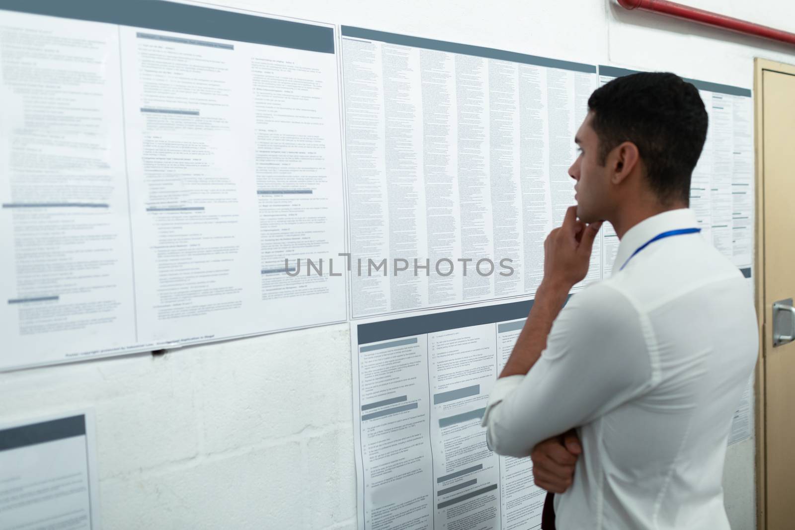 Side view of handsome young mixed-race male supervisor looking at inventory records on wall. This is a freight transportation and distribution warehouse. Industrial and industrial workers concept