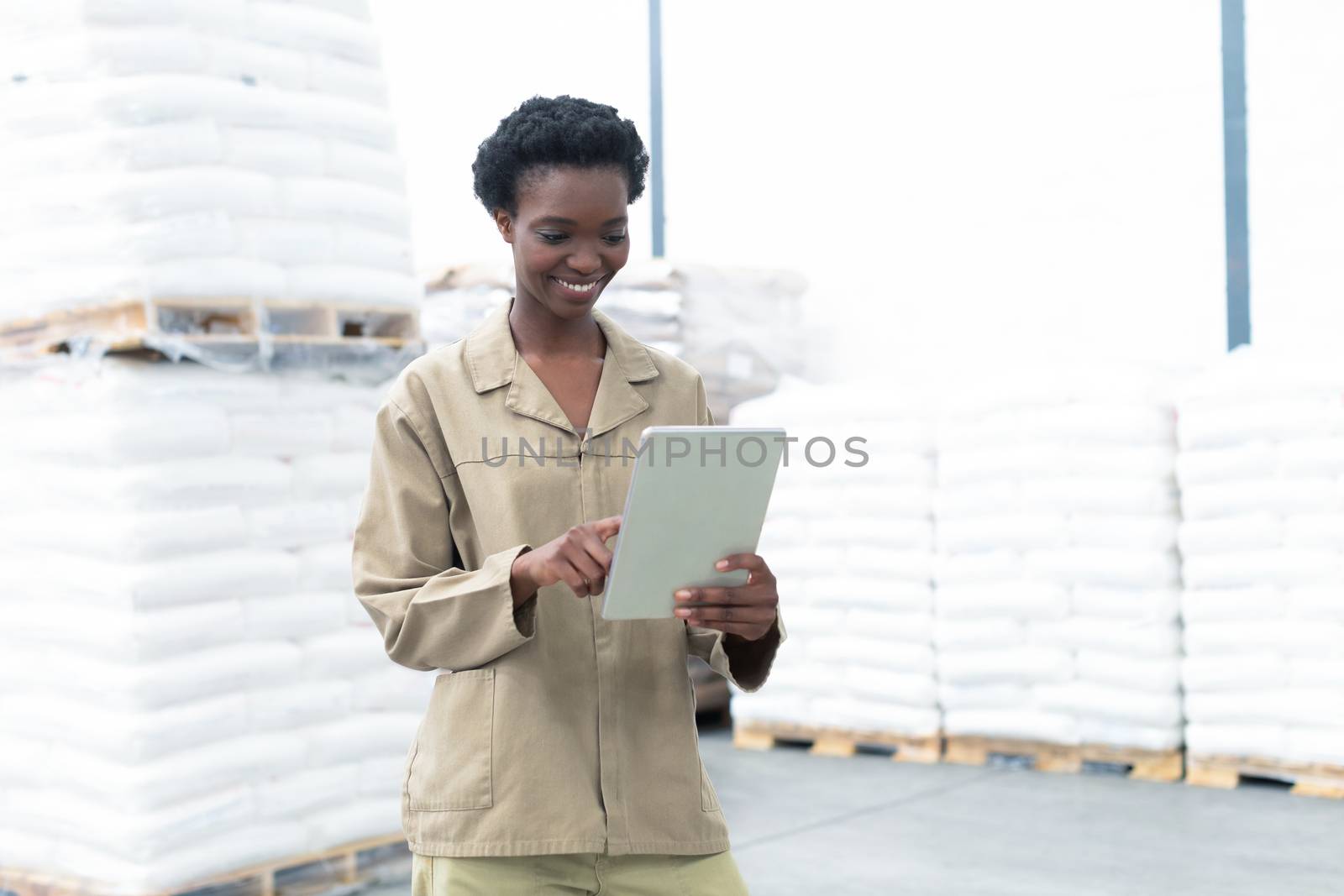 Front view of beautiful young African-american female worker working on digital tablet in warehouse. This is a freight transportation and distribution warehouse. Industrial and industrial workers concept