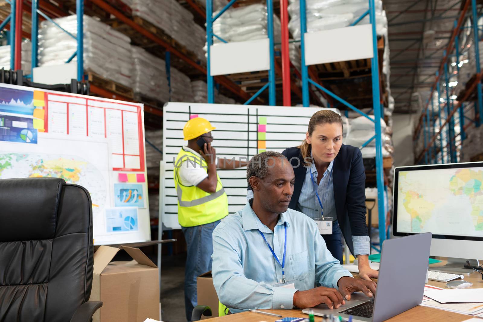 Front view of mature Caucasian female manager and African-american male supervisor working together on laptop at desk in warehouse. This is a freight transportation and distribution warehouse. Industrial and industrial workers concept