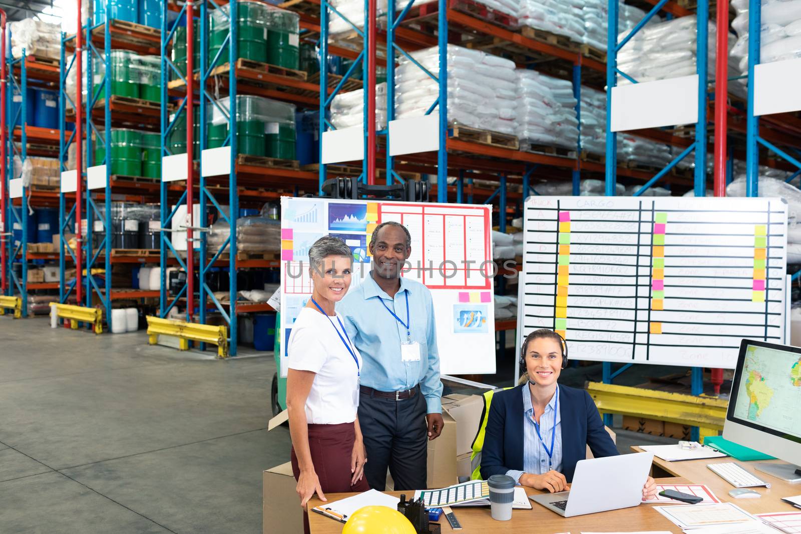 Portrait of beautiful Caucasian female manager with her coworkers discussing over laptop at desk in warehouse. This is a freight transportation and distribution warehouse. Industrial and industrial workers concept