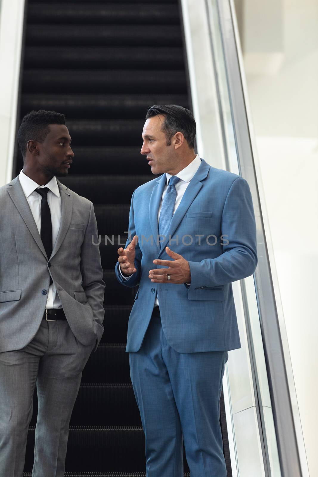 African-american young male executive talking with mature male executive in escalator by Wavebreakmedia