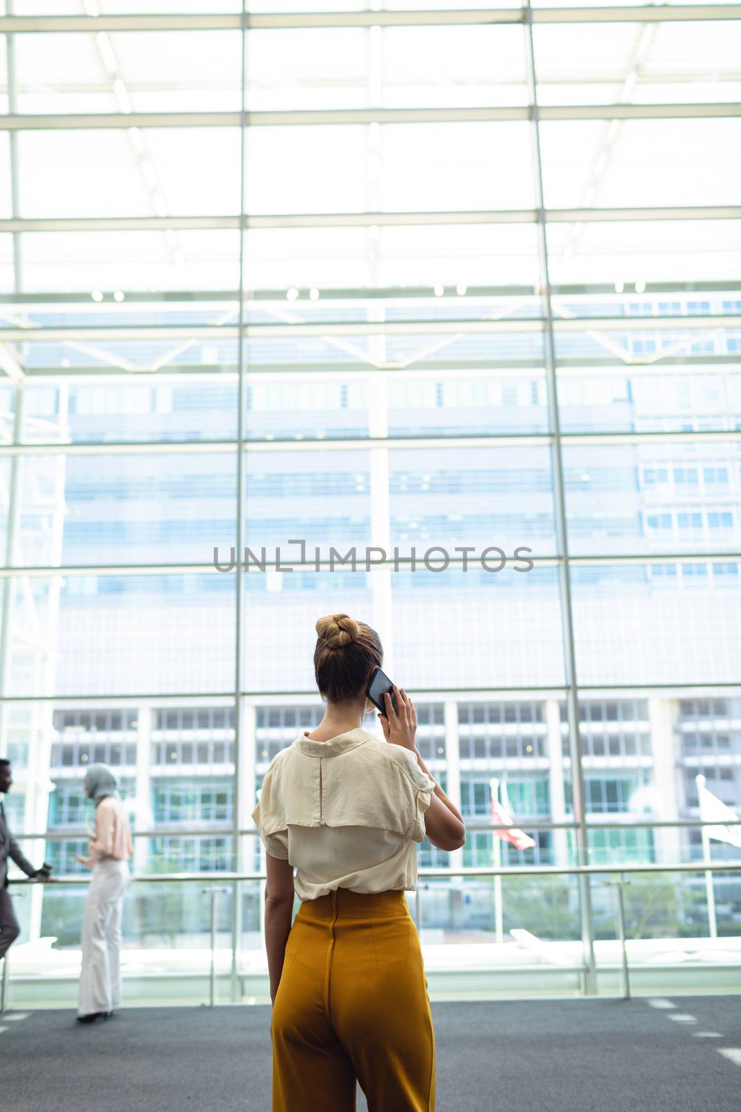 Rear view of young female executive looking outside in office while calling
