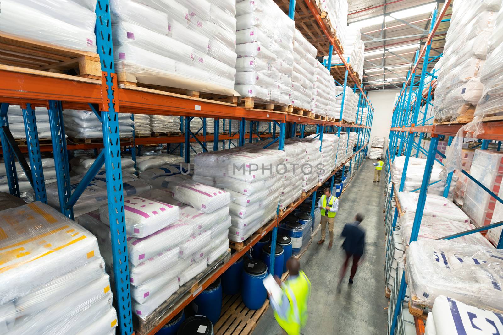 High angle view of diverse warehouse staff checking stocks in aisle in warehouse. They are holding clipboards and writing in it. This is a freight transportation and distribution warehouse. Industrial and industrial workers concept