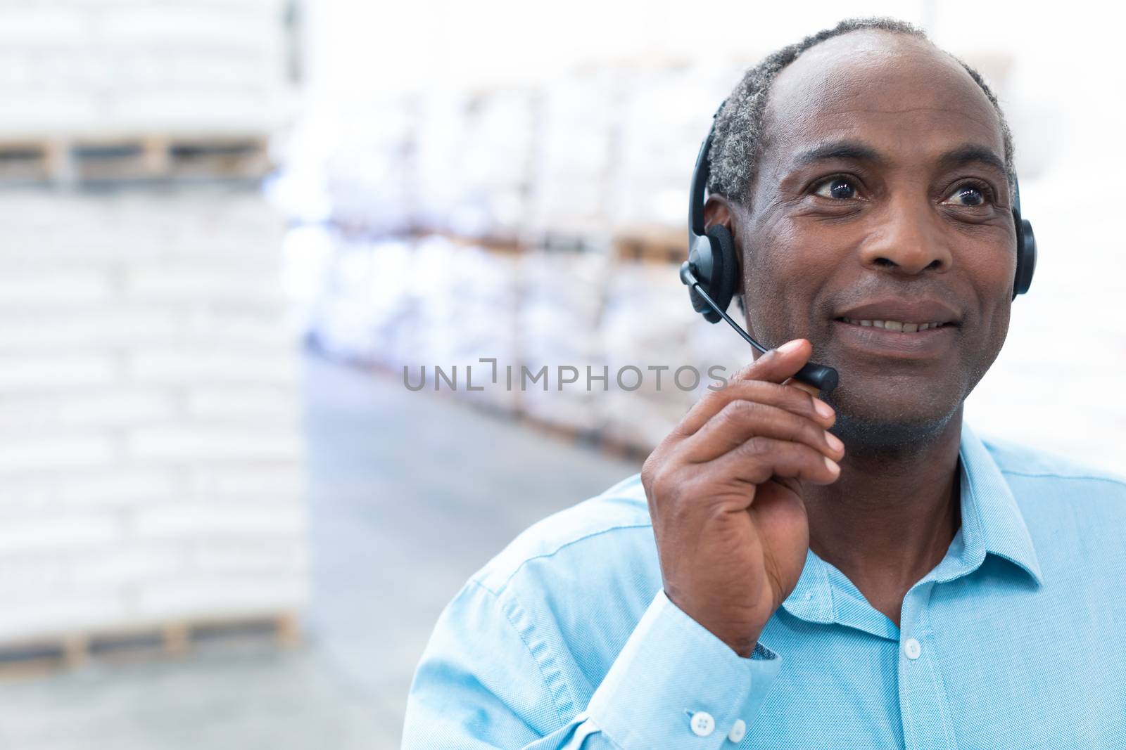 Portrait close-up of handsome mature African-american male supervisor talking on headset in warehouse. This is a freight transportation and distribution warehouse. Industrial and industrial workers concept