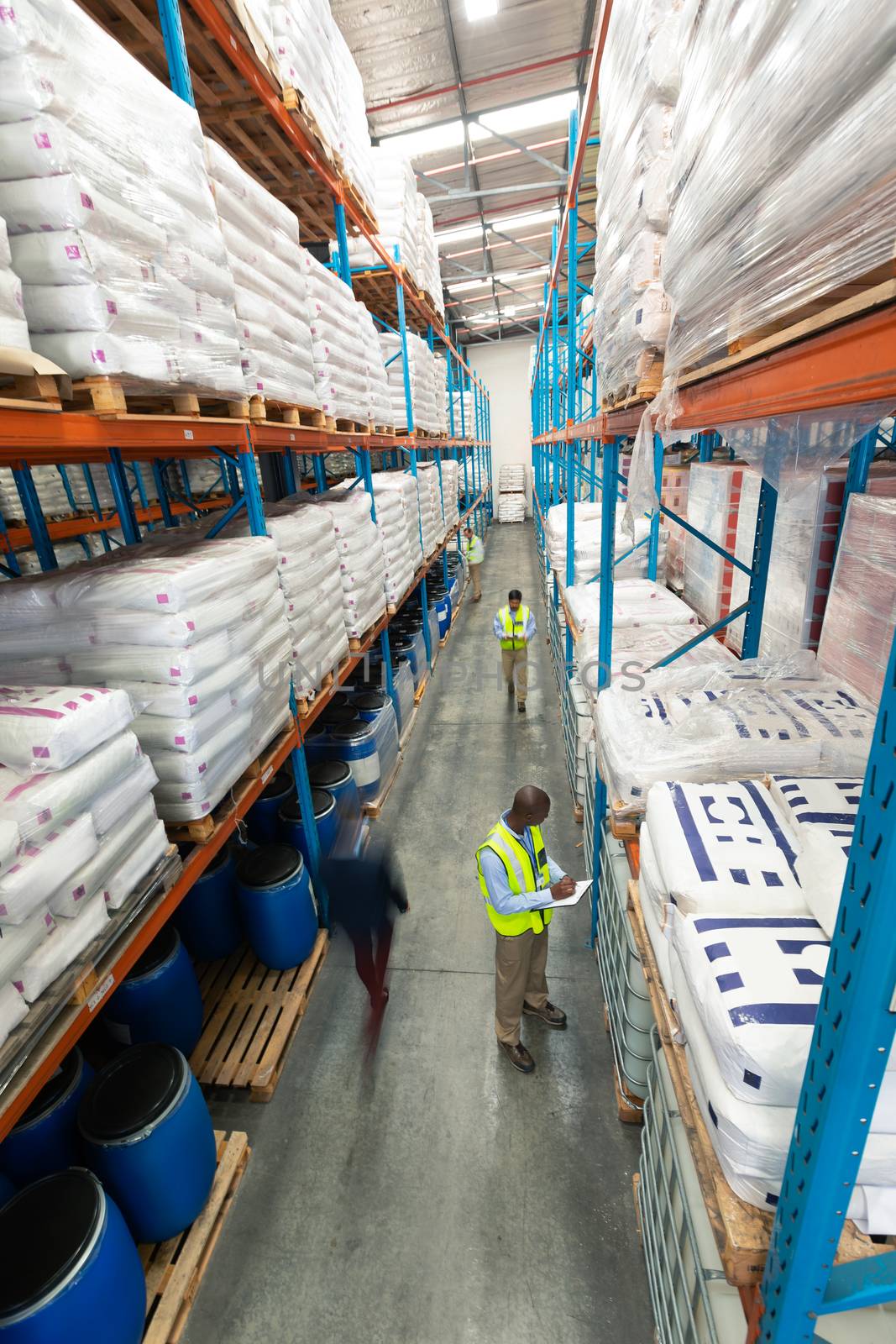 High angle view of diverse warehouse staff checking stocks in aisle in warehouse. They are holding clipboards and writing in it. This is a freight transportation and distribution warehouse. Industrial and industrial workers concept