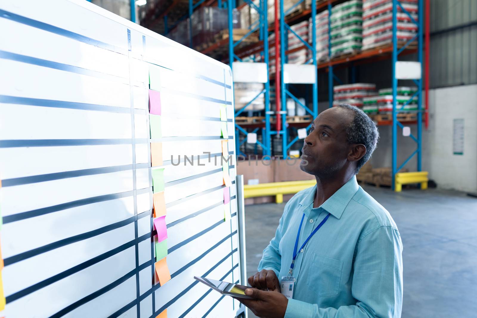 Side view of handsome mature African American male supervisor looking at whiteboard in warehouse. This is a freight transportation and distribution warehouse. Industrial and industrial workers concept