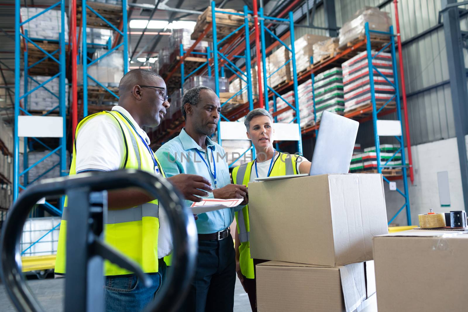 Side view of mature diverse warehouse staffs discussing over laptop in warehouse. This is a freight transportation and distribution warehouse. Industrial and industrial workers concept