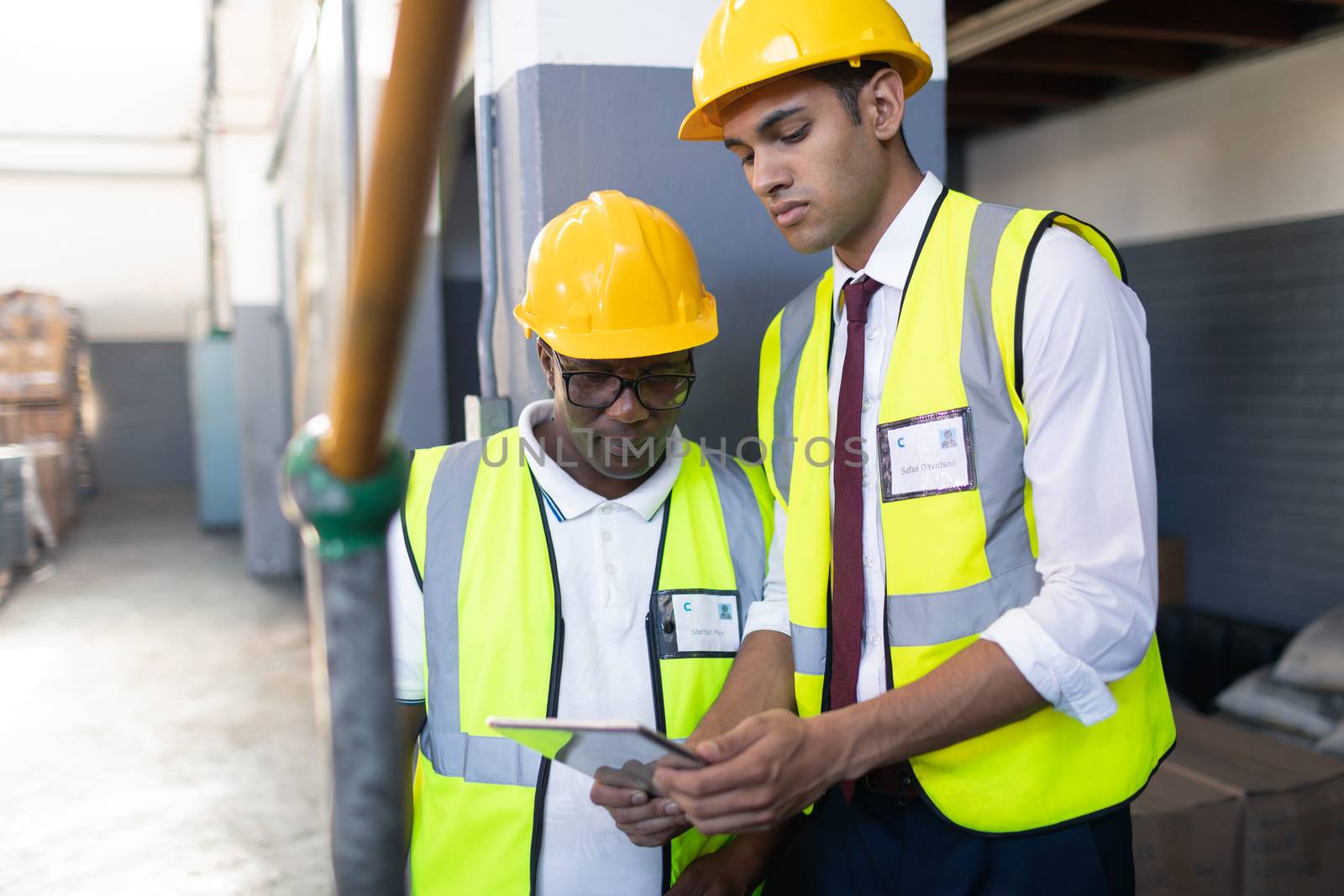 Front view of African-american male supervisor with his African-american coworker discussing over digital tablet in warehouse. This is a freight transportation and distribution warehouse. Industrial and industrial workers concept