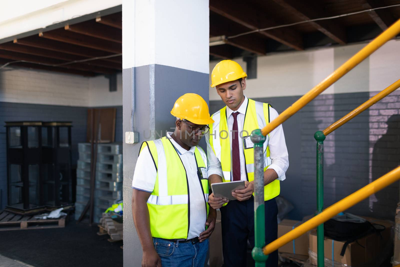 Front view of African-american Male supervisor with his African-american coworker discussing over digital tablet in warehouse. This is a freight transportation and distribution warehouse. Industrial and industrial workers concept