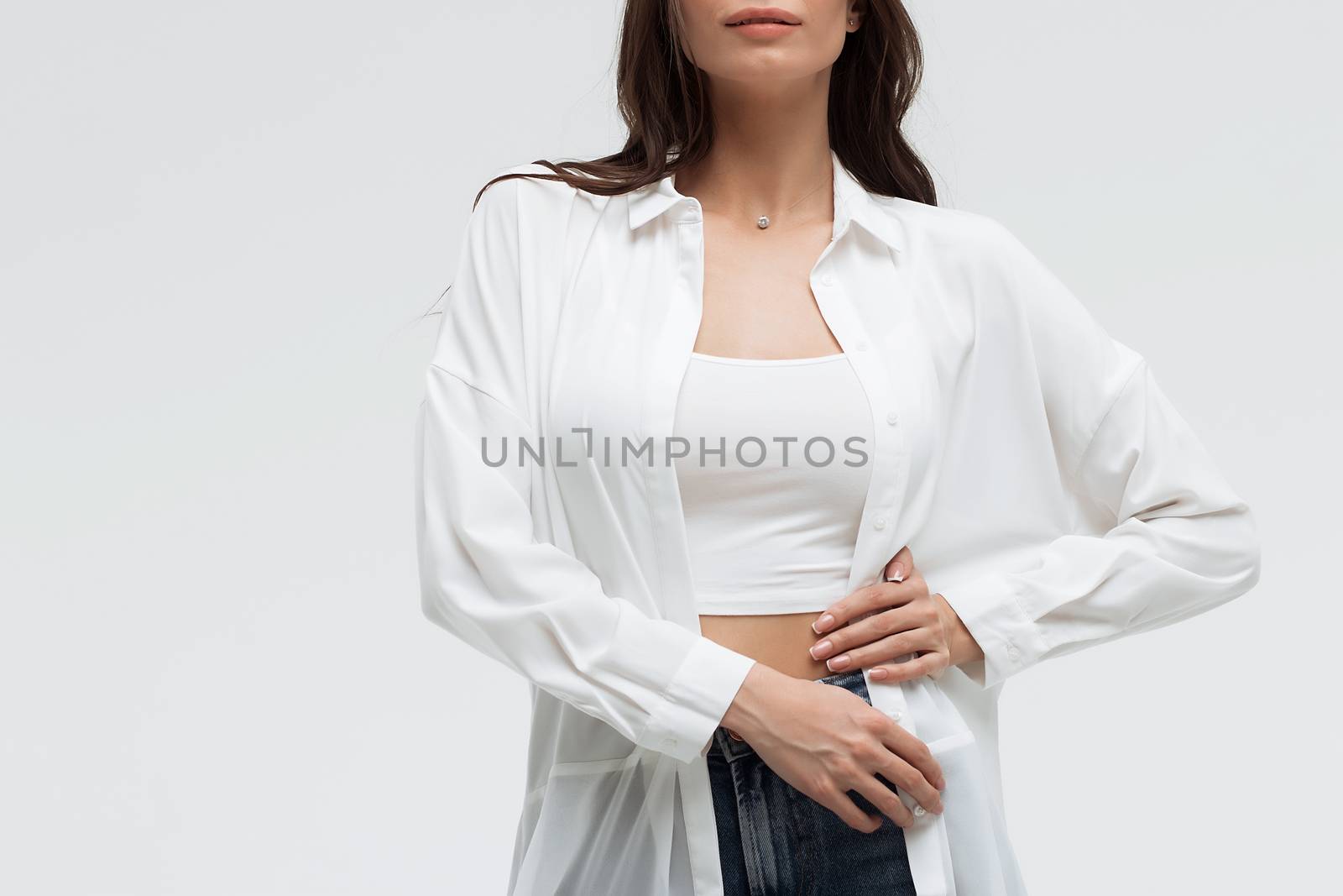 Crop confident long haired woman in white shirt and lingerie and jeans with crossed hands on white background