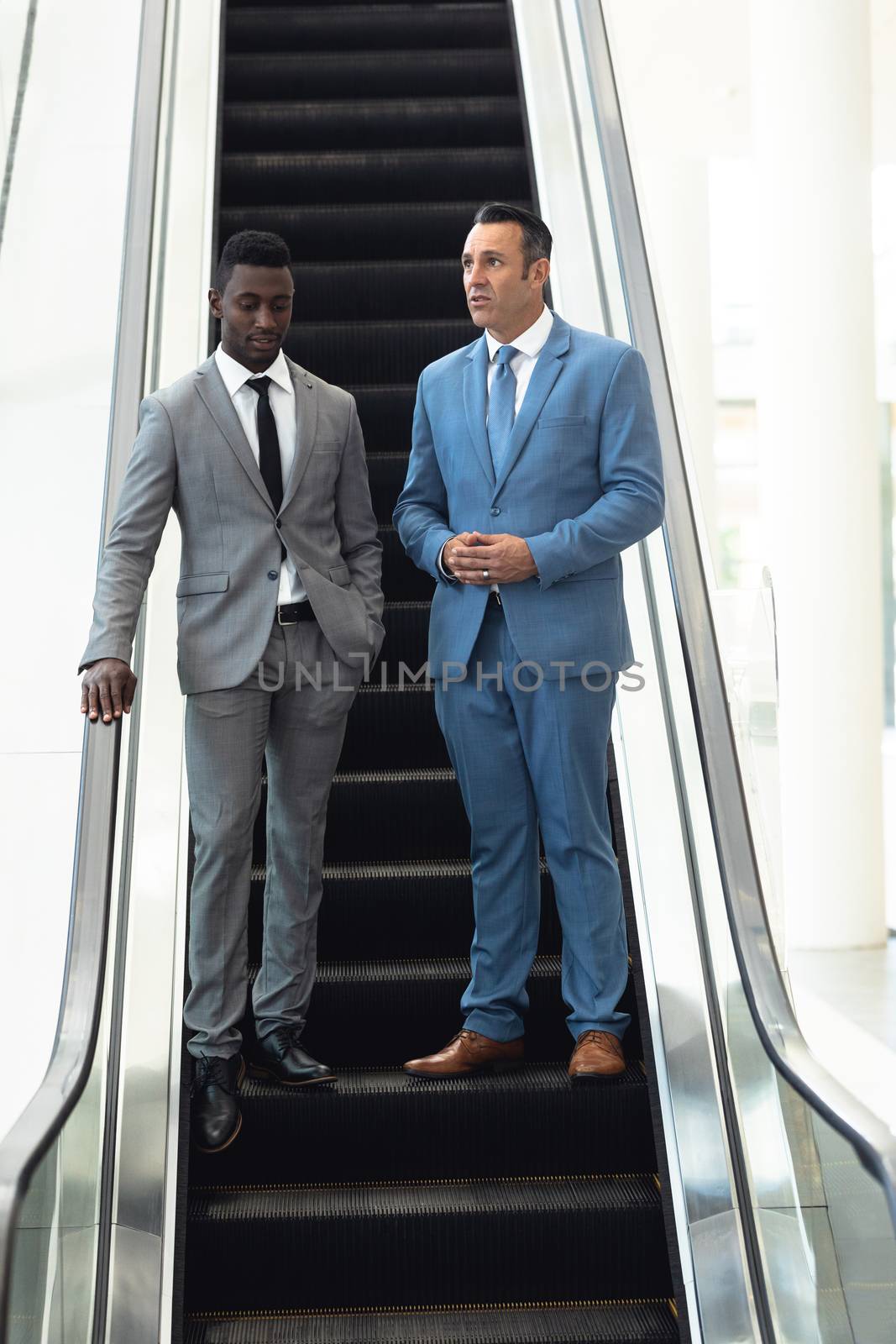 Front view of African-american young male executive talking with mature male executive in escalator