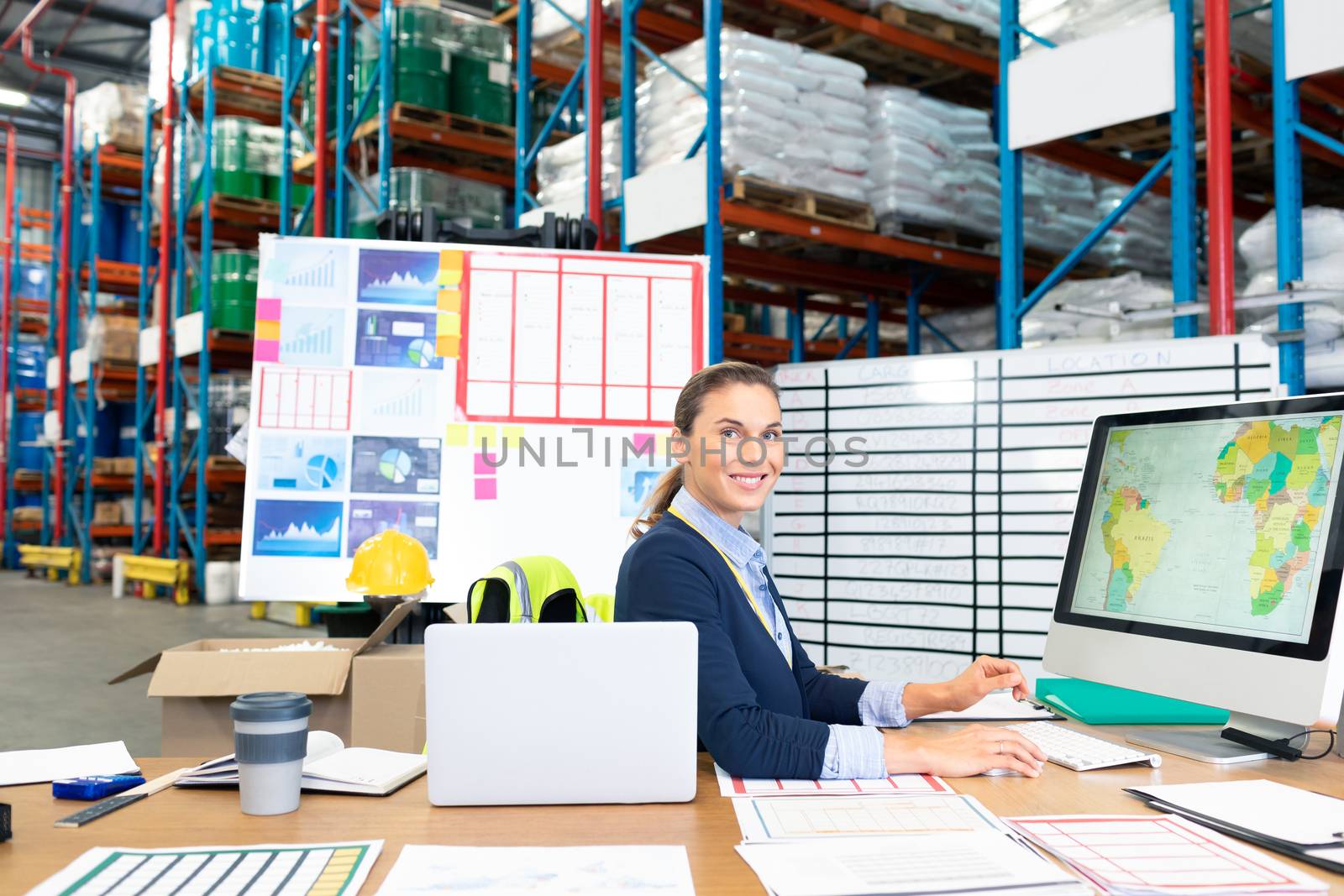 Portrait of beautiful Caucasian female manager working on computer at desk in warehouse. This is a freight transportation and distribution warehouse. Industrial and industrial workers concept