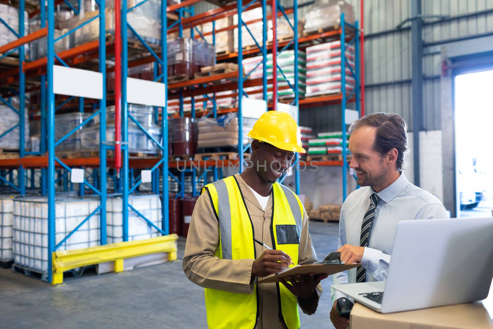 Front view of happy diverse staffs discussing over clipboard in warehouse. This is a freight transportation and distribution warehouse. Industrial and industrial workers concept