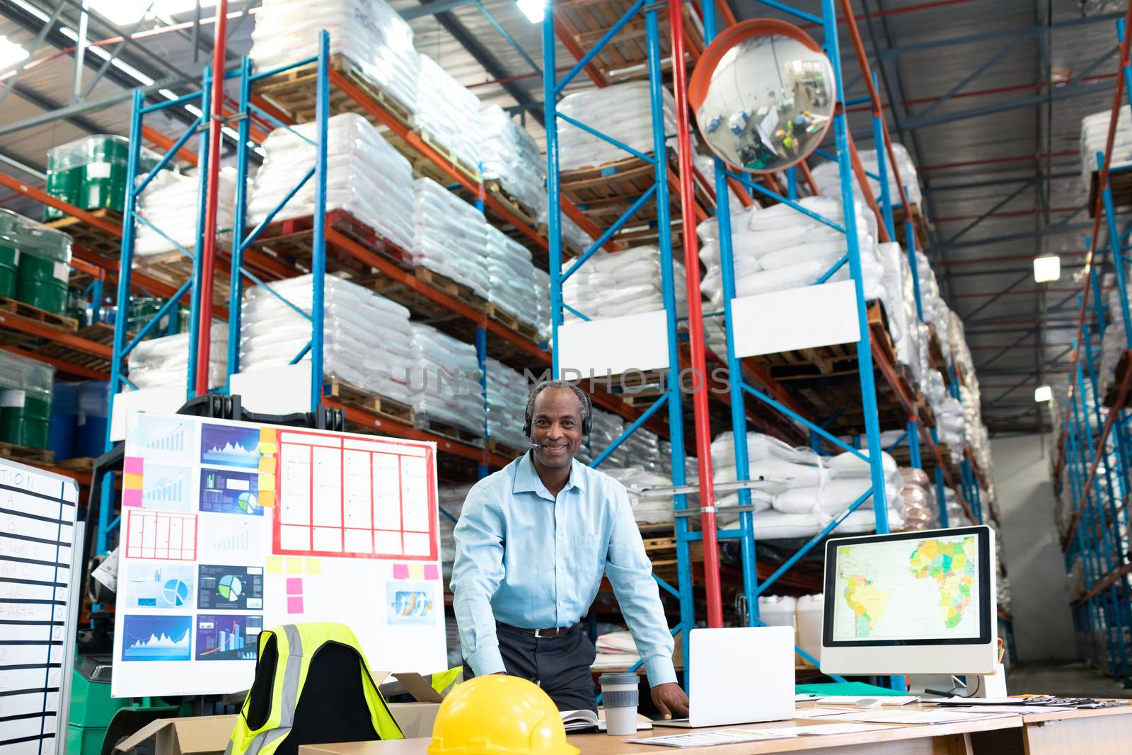 Portrait of handsome mature African-american male supervisor smiling at desk in warehouse. This is a freight transportation and distribution warehouse. Industrial and industrial workers concept