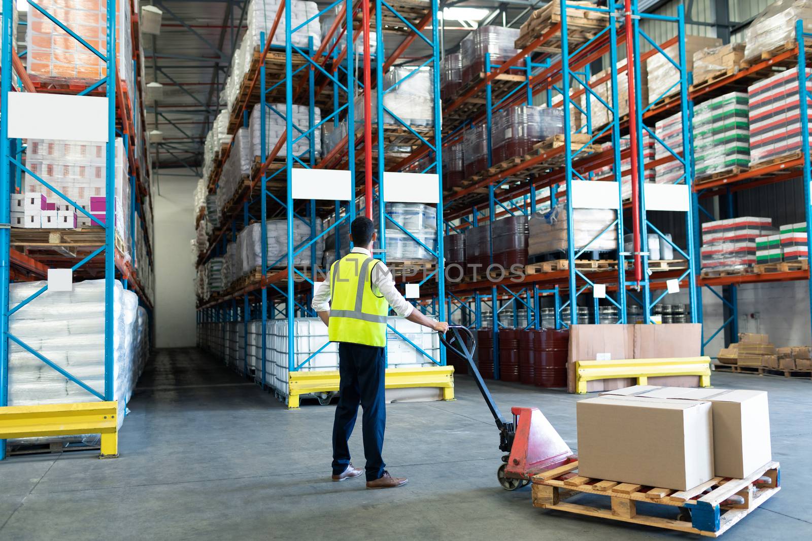 Rear view of Caucasian male staff using pallet jack in warehouse. This is a freight transportation and distribution warehouse. Industrial and industrial workers concept