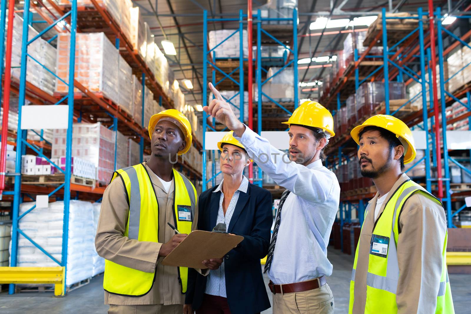 Front view of Caucasian male supervisor standing with diverse coworkers and pointing at distance in warehouse. This is a freight transportation and distribution warehouse. Industrial and industrial workers concept