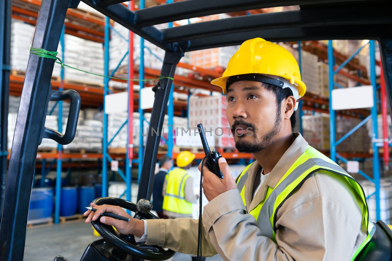 Male worker talking on walkie-talkie while driving forklift in warehouse by Wavebreakmedia
