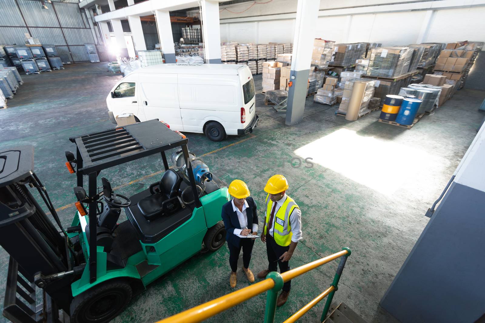 High angle view of Caucasian female manager and male supervisor discussing over clipboard in warehouse. This is a freight transportation and distribution warehouse. Industrial and industrial workers concept