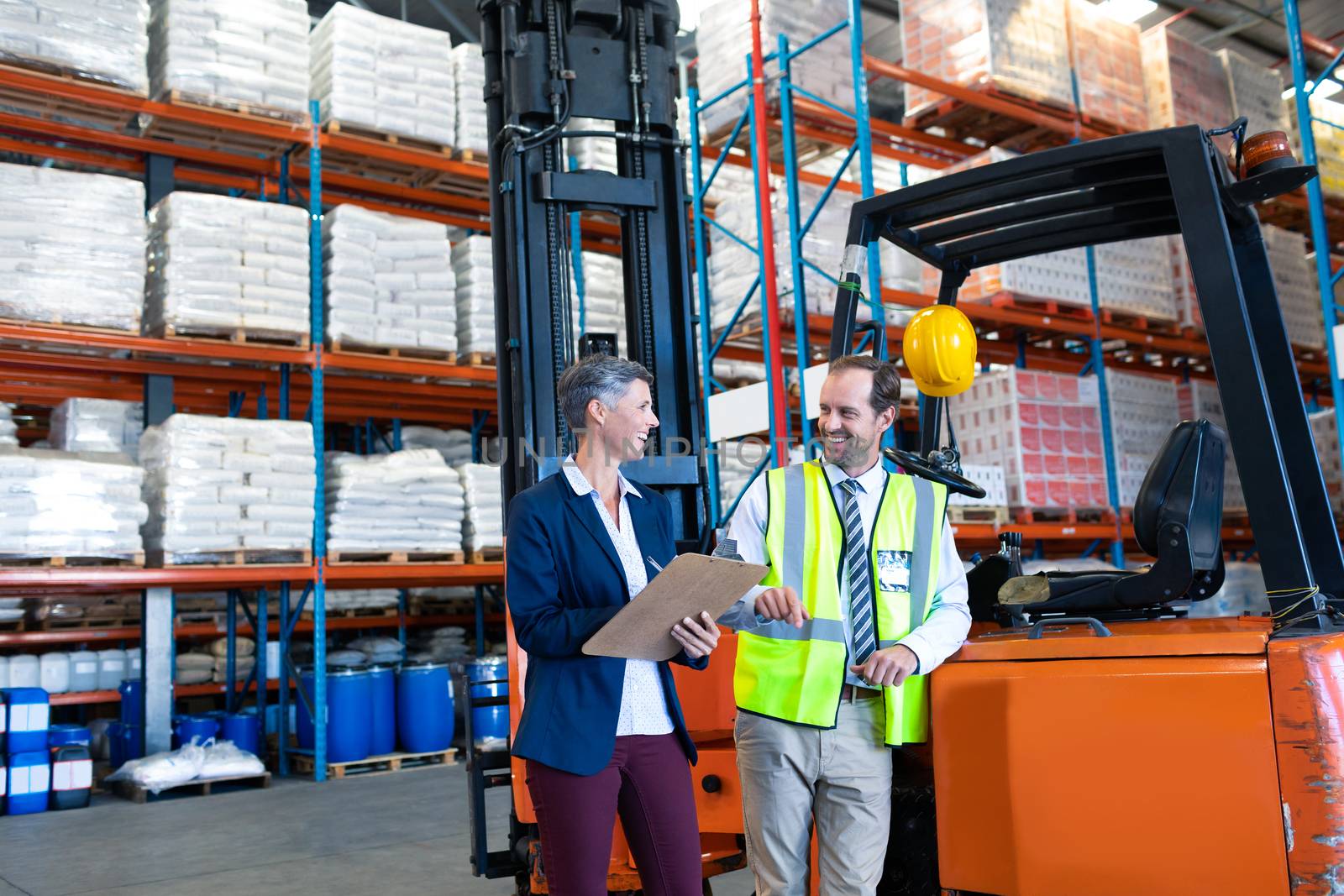 Male and female staff interacting with each other near forklift in warehouse by Wavebreakmedia