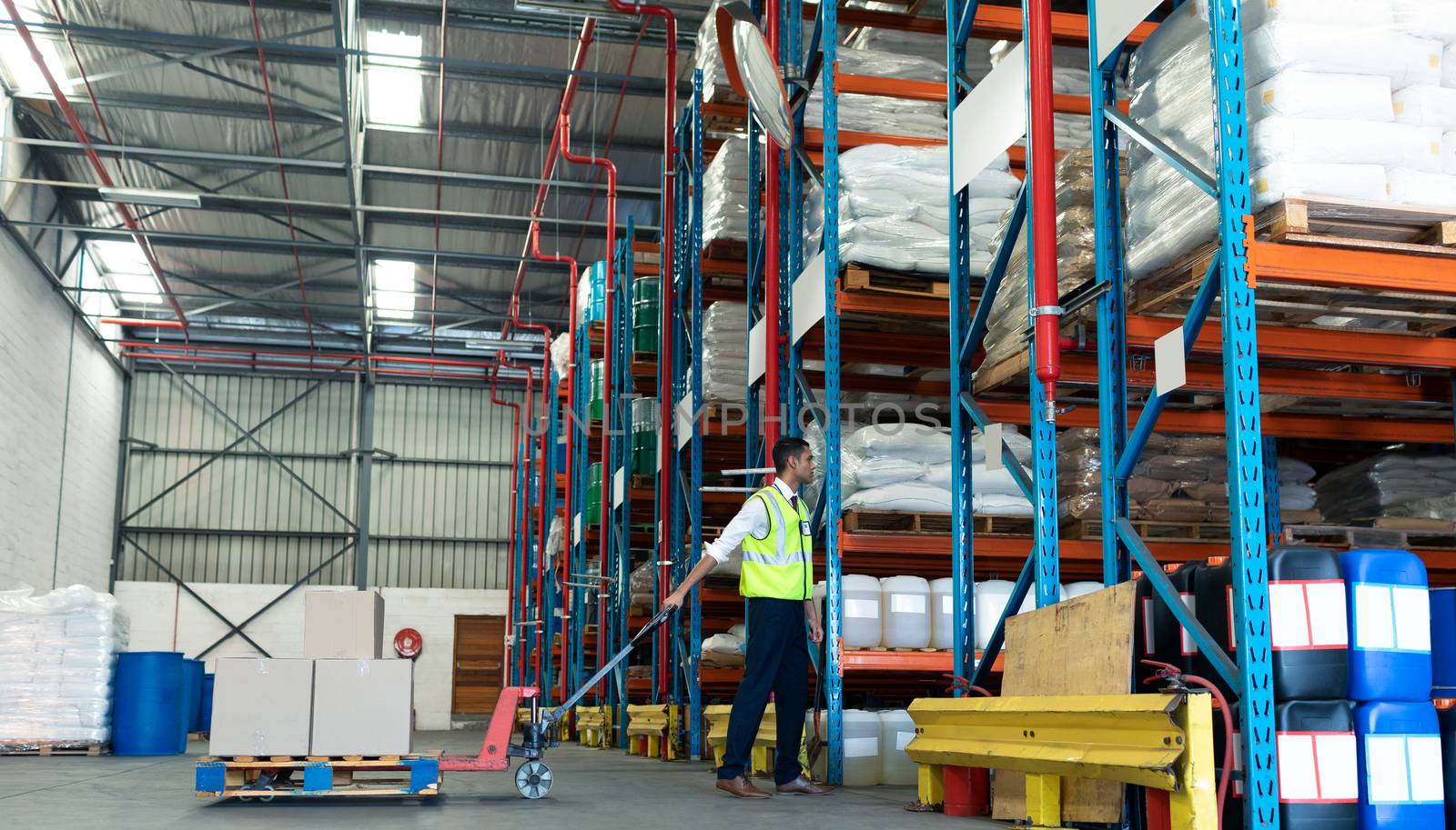 Side view of Young Caucasian male staff using pallet jack in warehouse. This is a freight transportation and distribution warehouse. Industrial and industrial workers concept