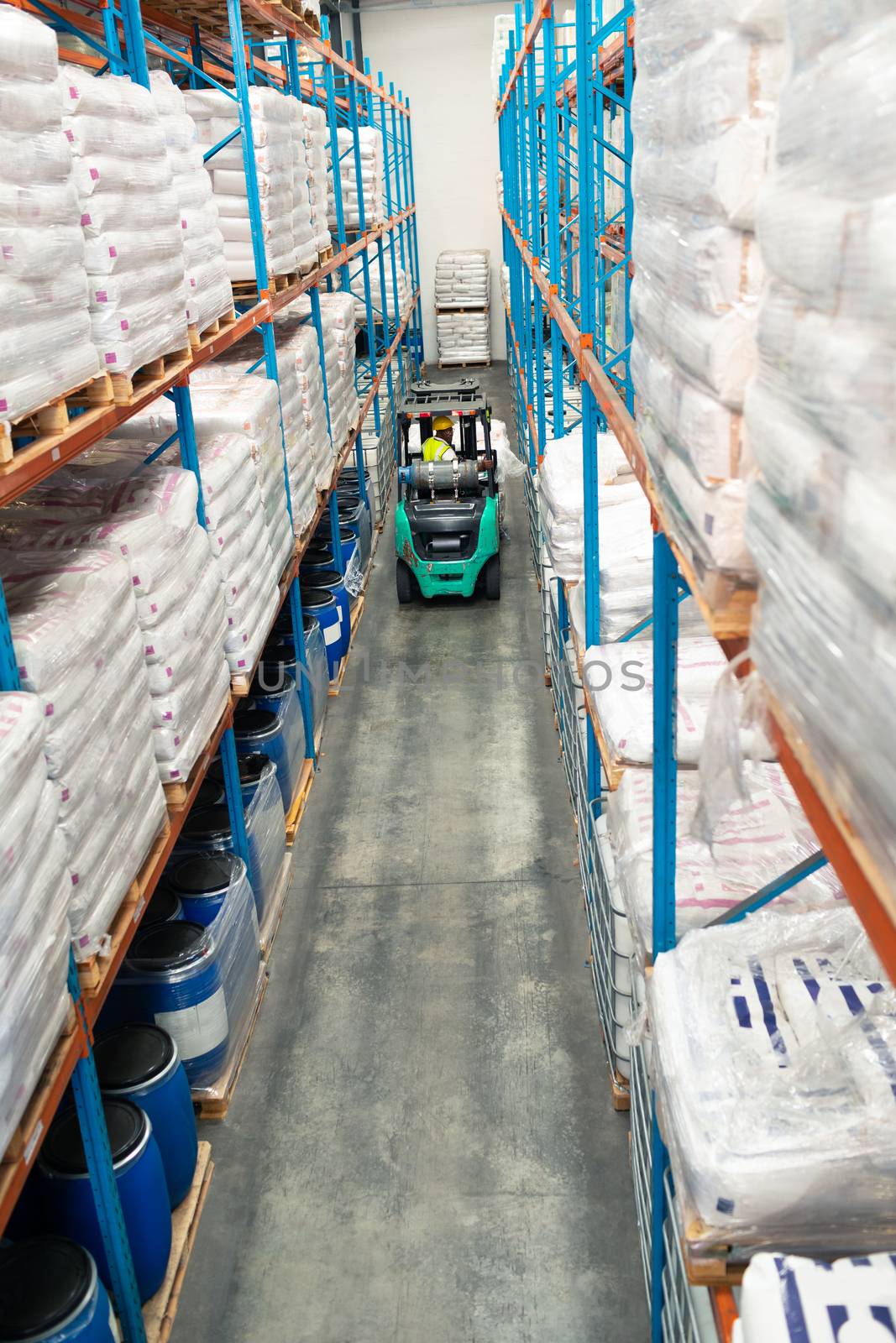 High angle view of African-american male worker driving forklift in warehouse. This is a freight transportation and distribution warehouse. Industrial and industrial workers concept