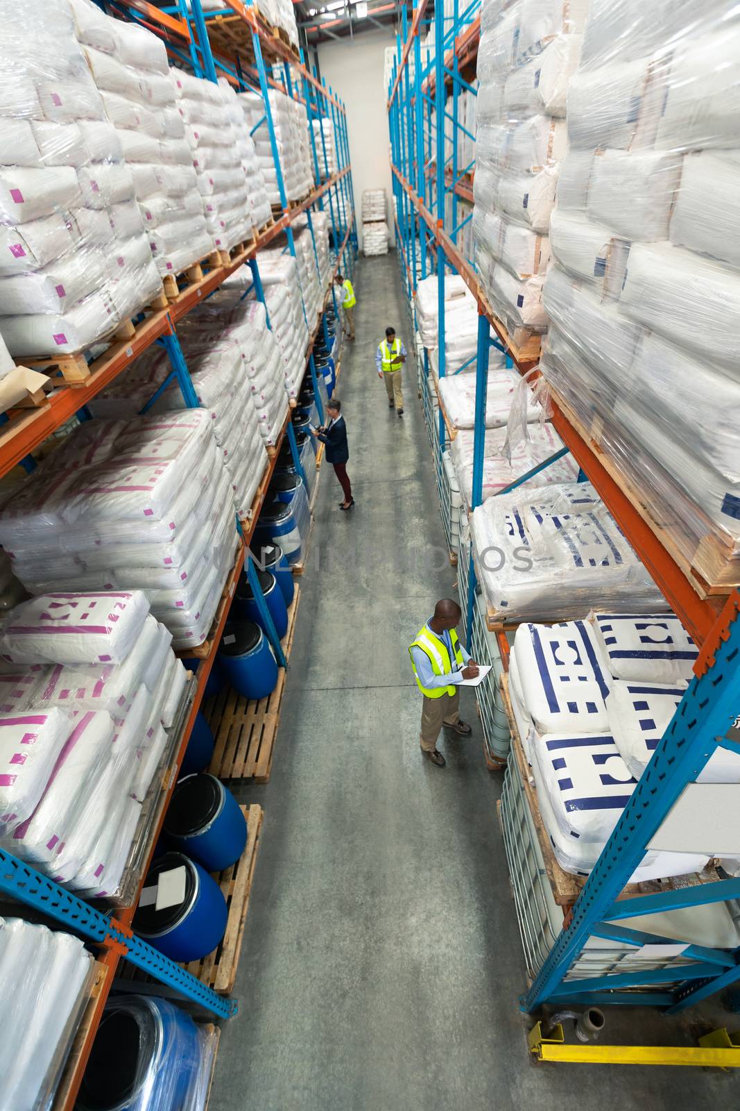 High angle of diverse warehouse staff checking stocks in aisle in warehouse. They are holding clipboards and writing in it. This is a freight transportation and distribution warehouse. Industrial and industrial workers concept