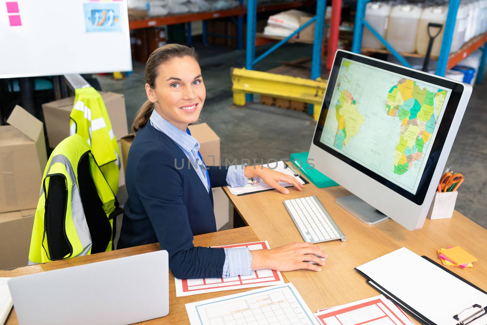 Portrait of beautiful young Caucasian female manager working on computer at desk in warehouse. This is a freight transportation and distribution warehouse. Industrial and industrial workers concept
